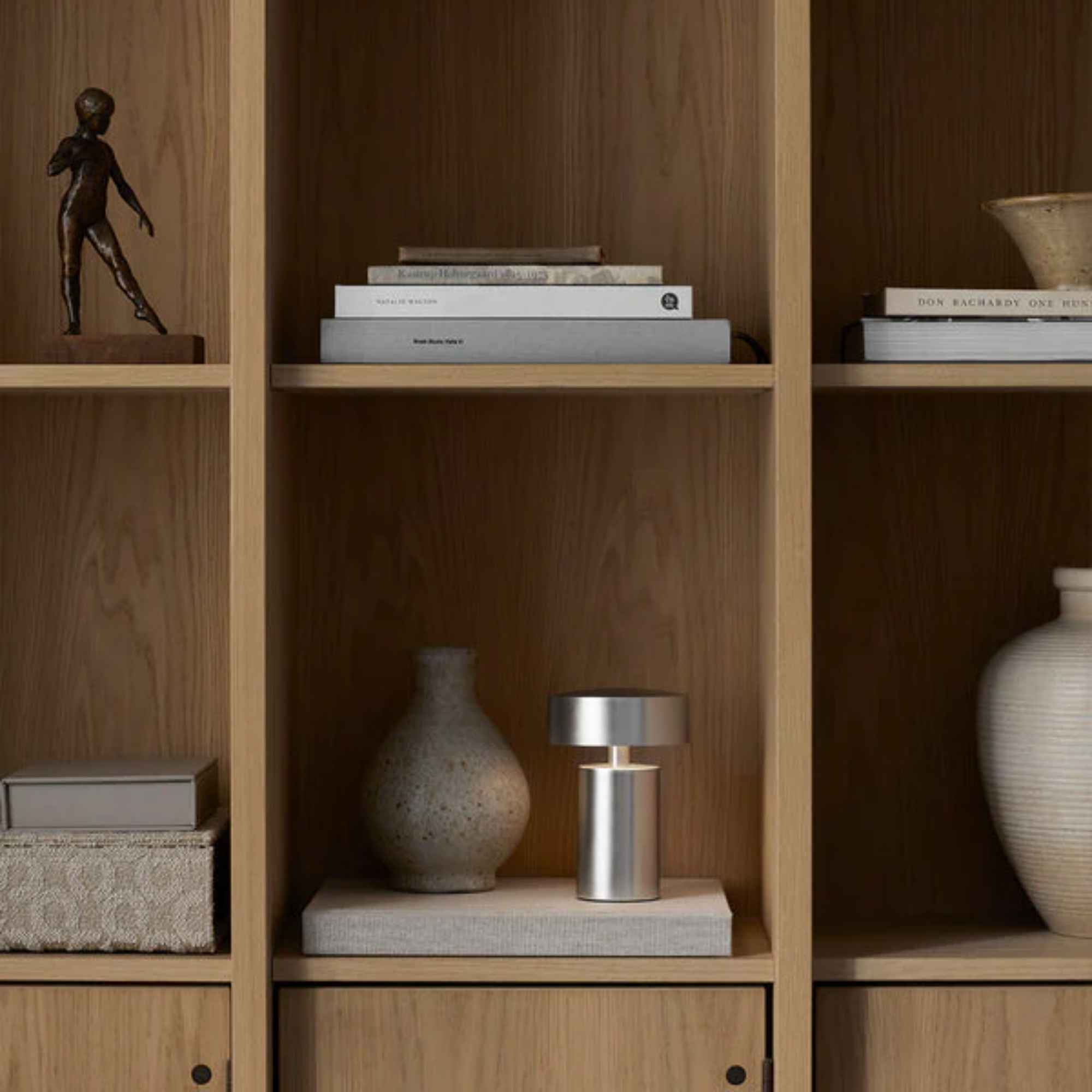 The brushed aluminum Column Portable Table Lamp from Audo Copenhagen in a home library on a bookshelf.