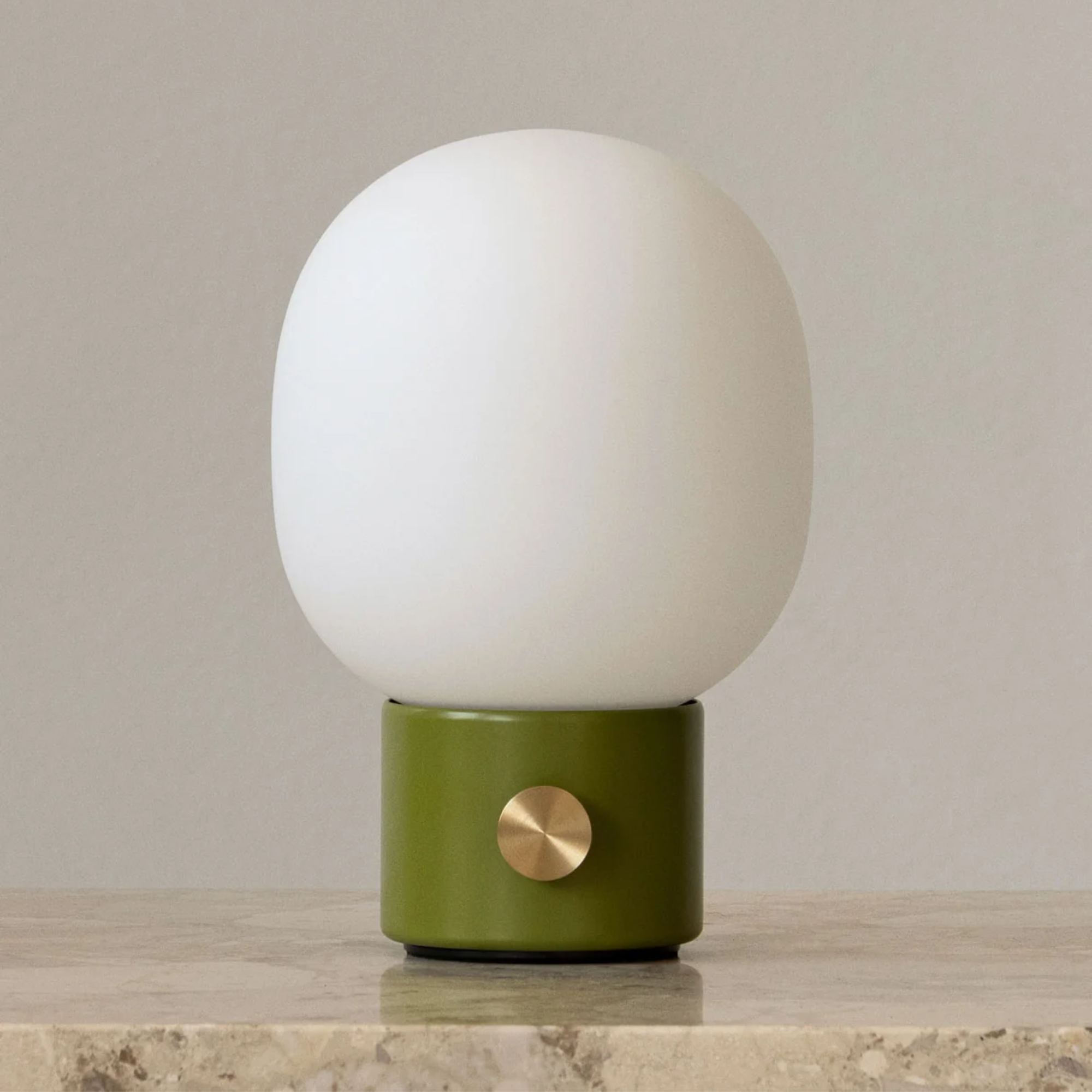 The dusty green JWDA Portable Table Lamp from Audo Copenhagen in a lounge on top of marble furniture.