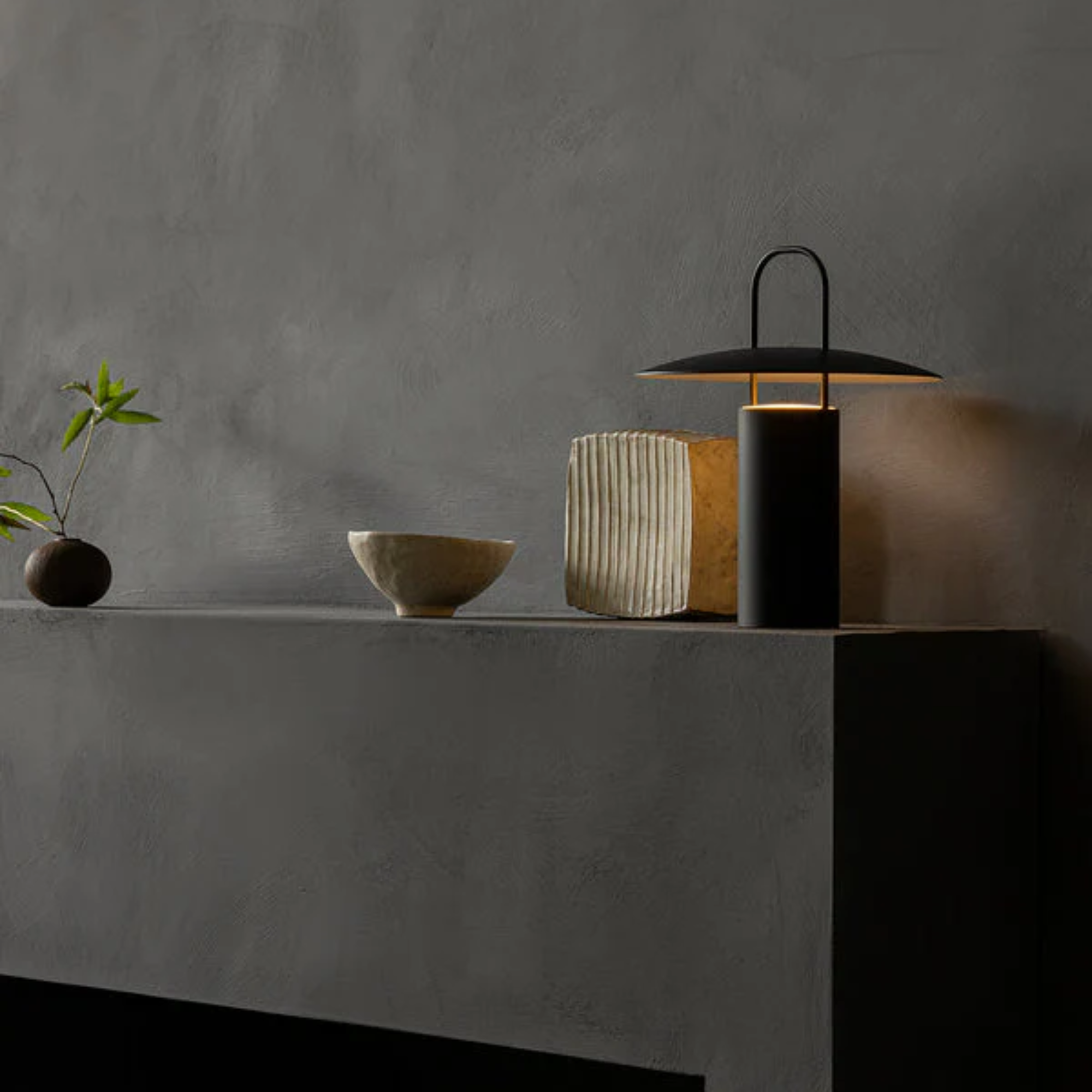 The black Ray Portable Table Lamp from Audo Copenhagen on top of a fireplace with other decor.