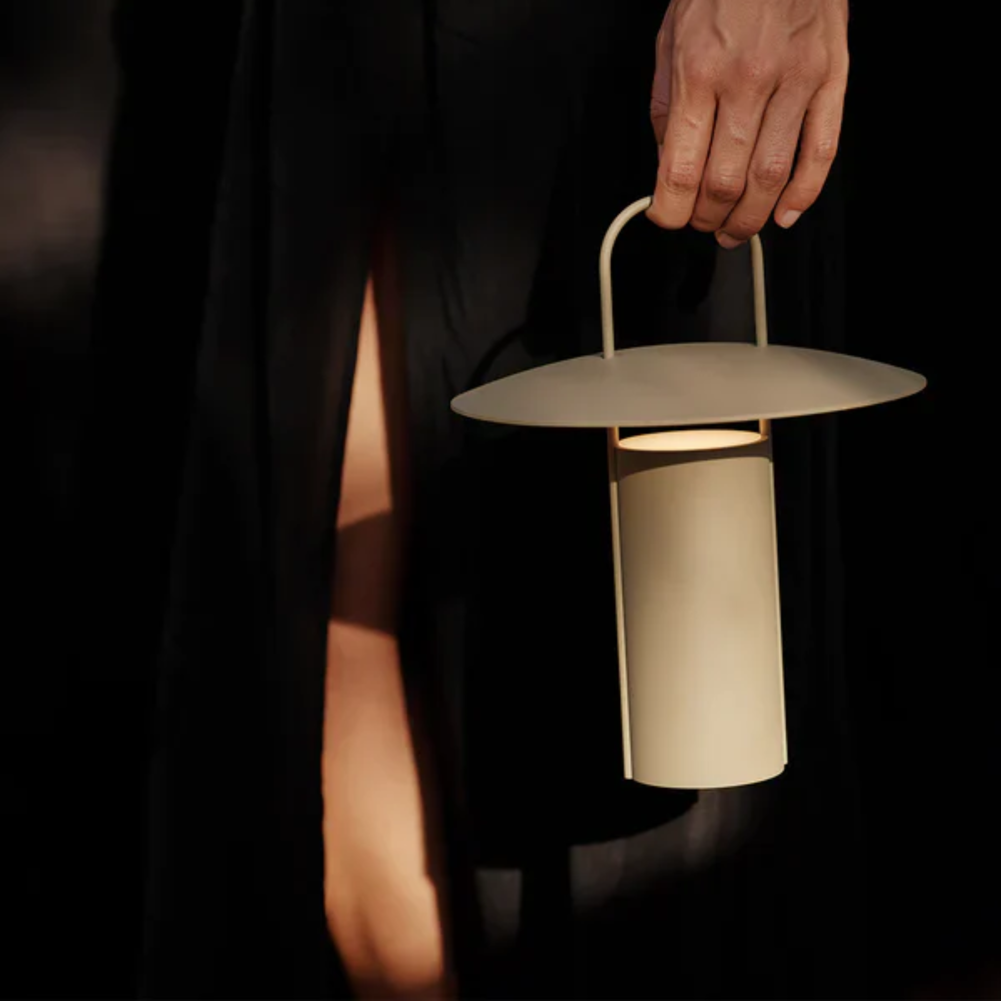 The dusty matte green Ray Portable Table Lamp from Audo Copenhagen handheld while outdoors.