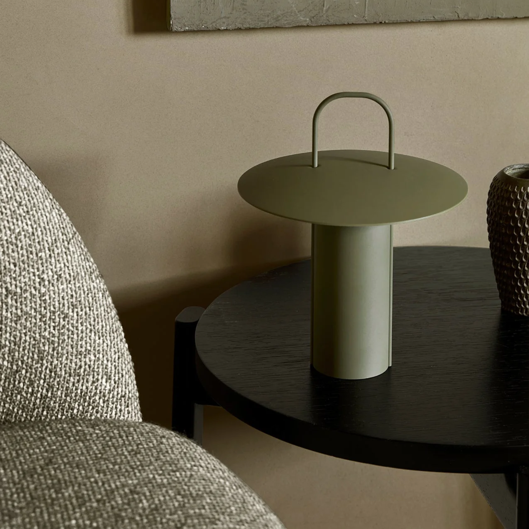 The dusty matte green Ray Portable Table Lamp from Audo Copenhagen in a living room on an end table beside a couch.