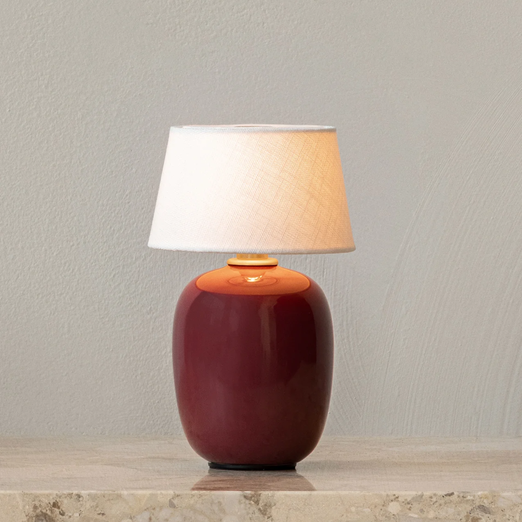 The ruby Torso Portable Table Lamp from Audo Copenhagen in a family area on top of a marble surface.