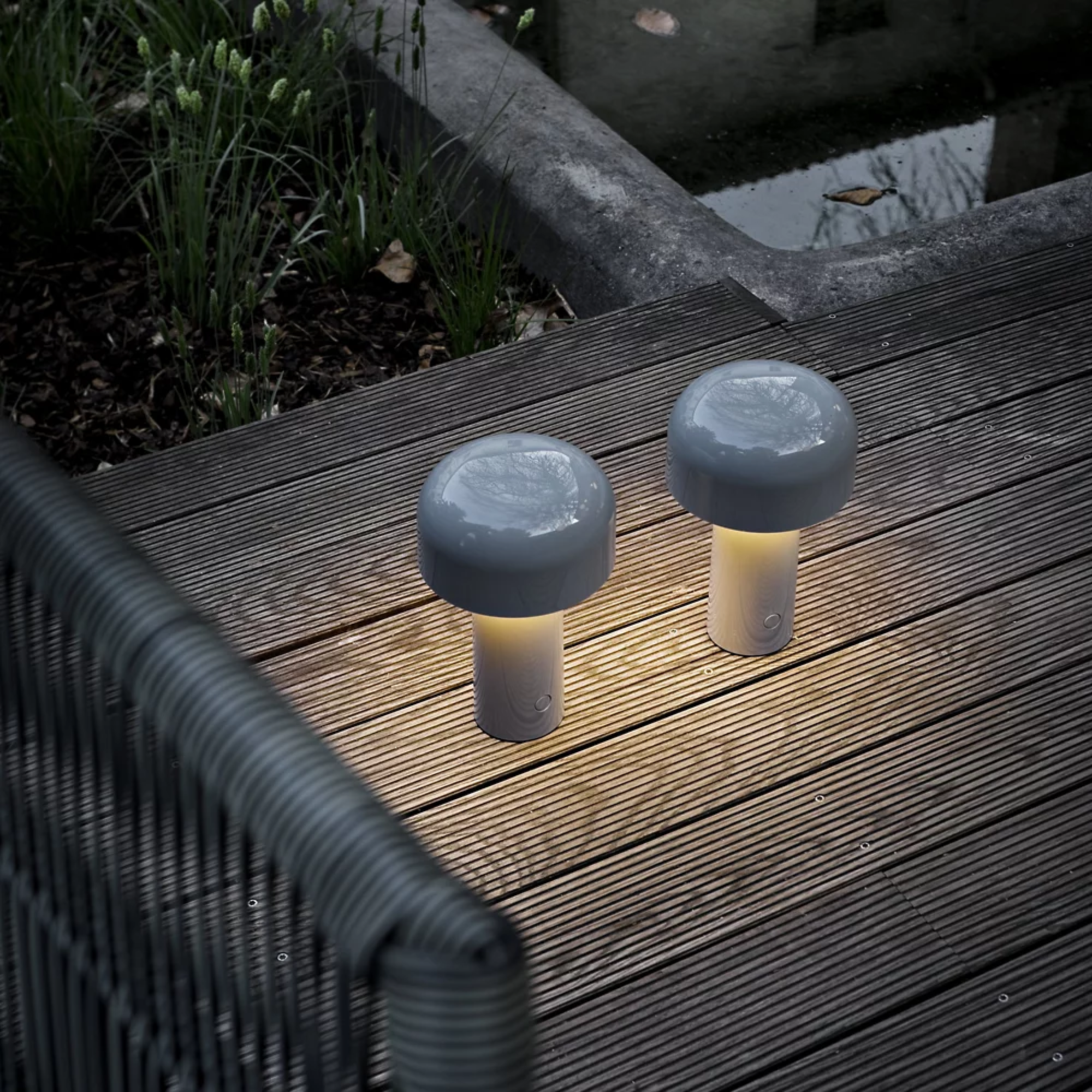The gray blue Bellhop Cordless Lamp from FLOS on a wooden porch outside.