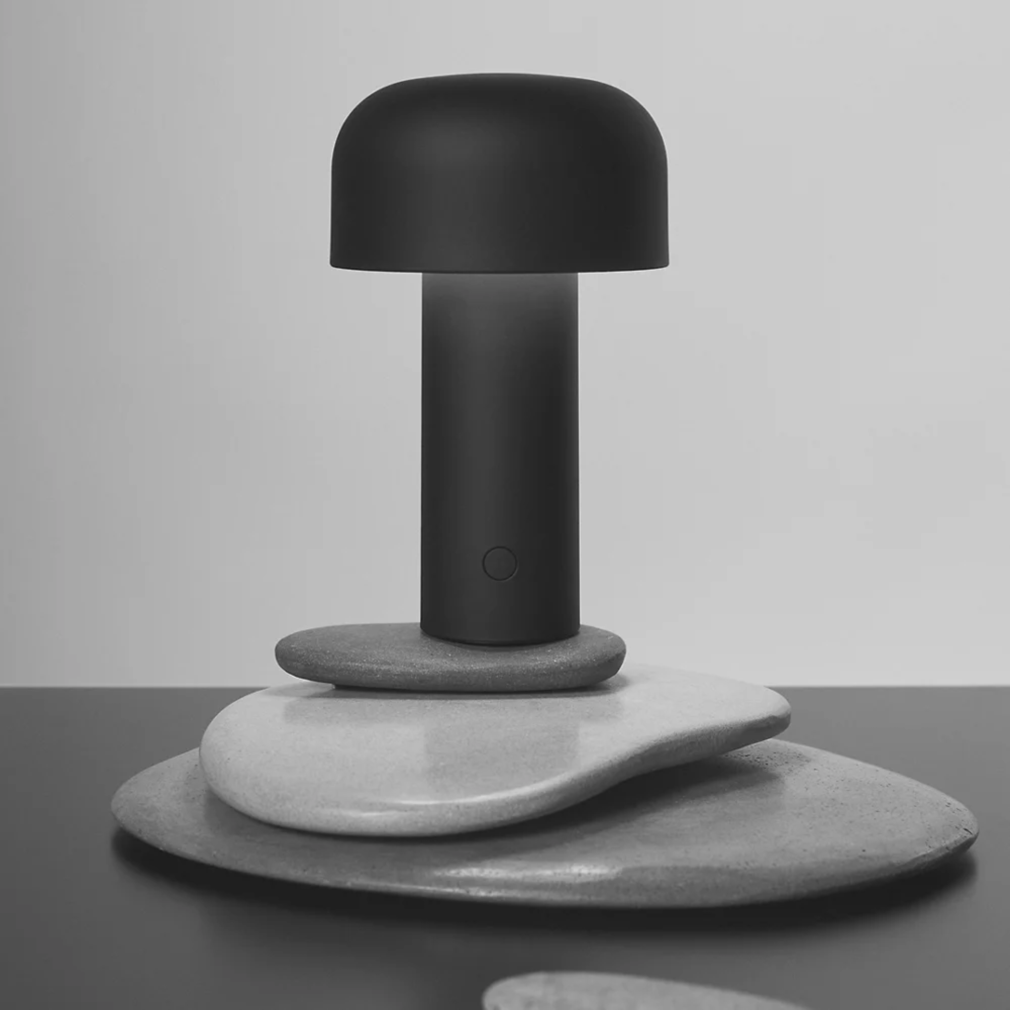 The matte black Bellhop Cordless Lamp from FLOS in a home office on top of stones.