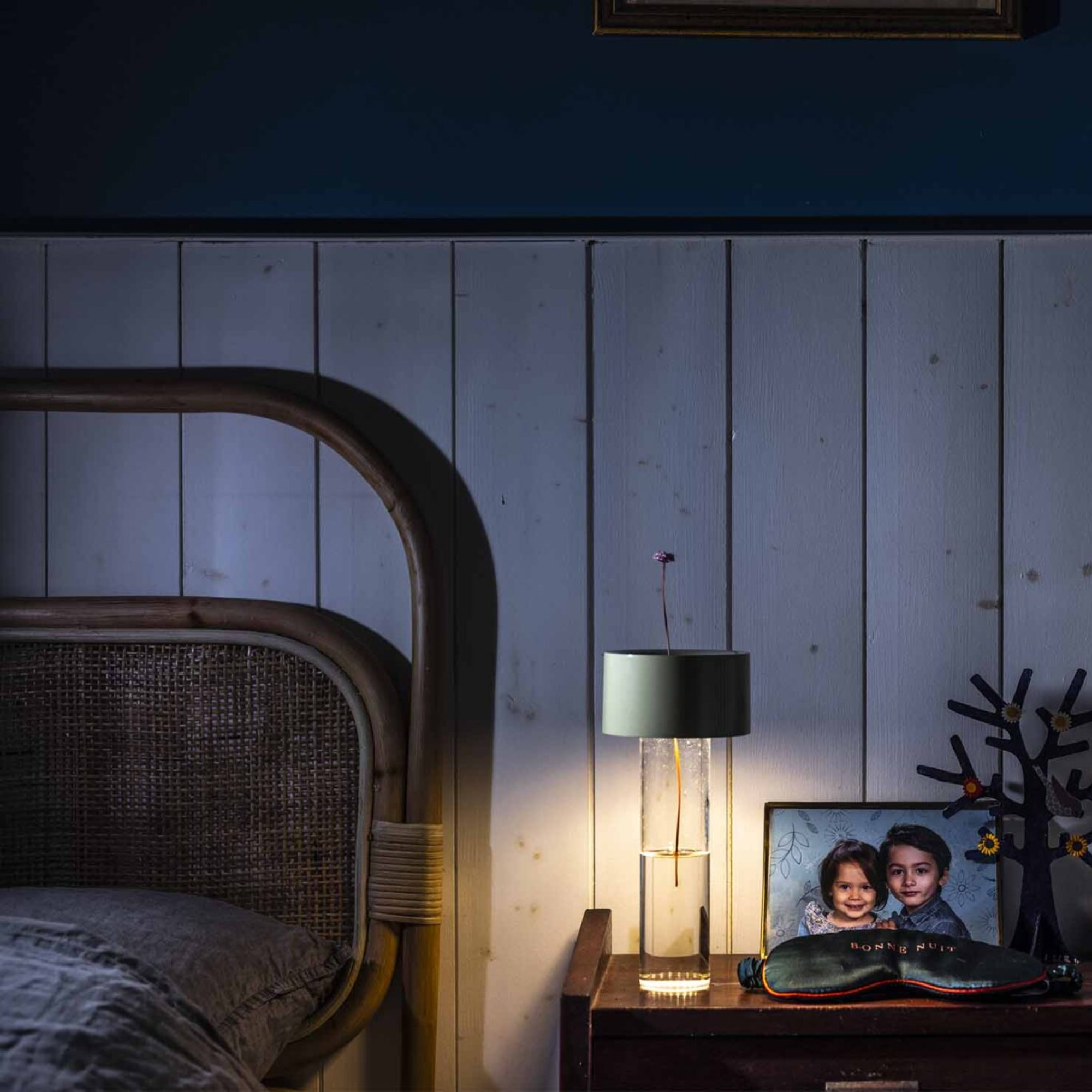 The sage green Fleur Portable Table Lamp from Foscarini in a bedroom on a bedside table next to a photograph.