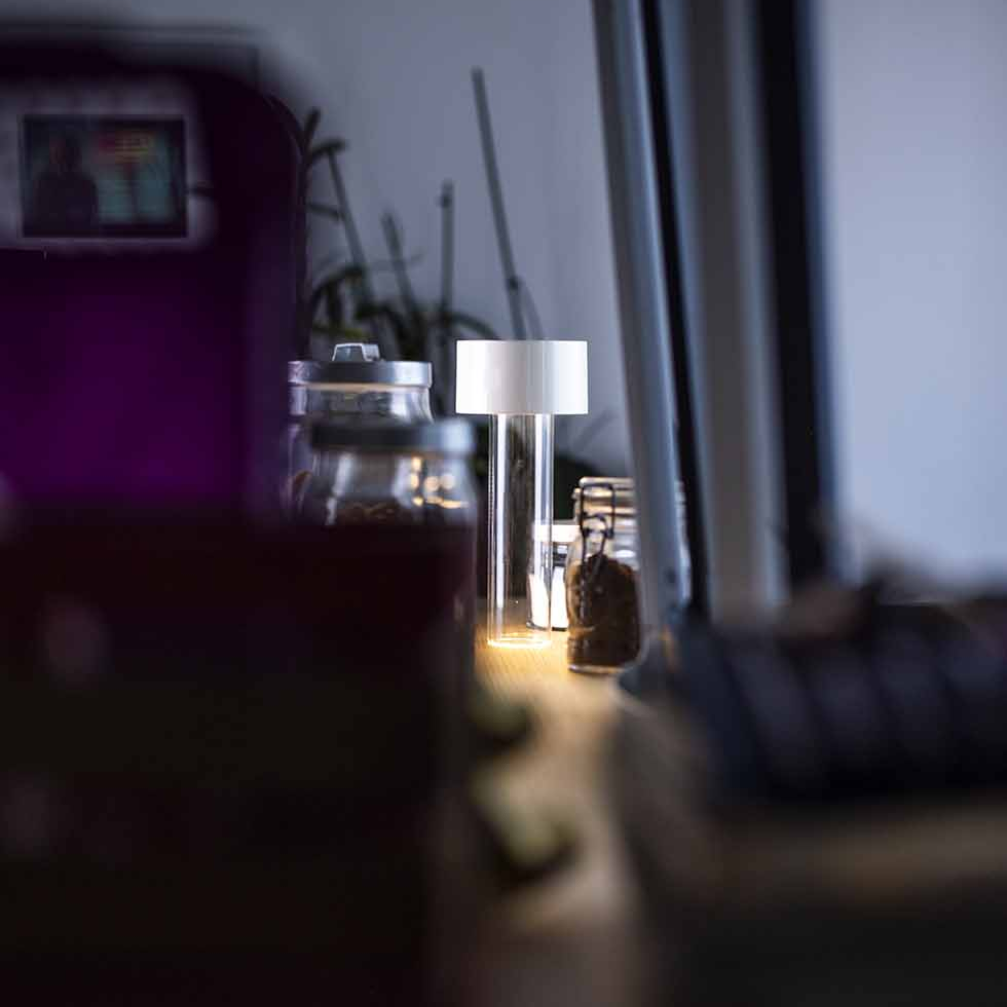 The white Fleur Portable Table Lamp from Foscarini in a kitchen beside various jars of herbs, coffee and spices.