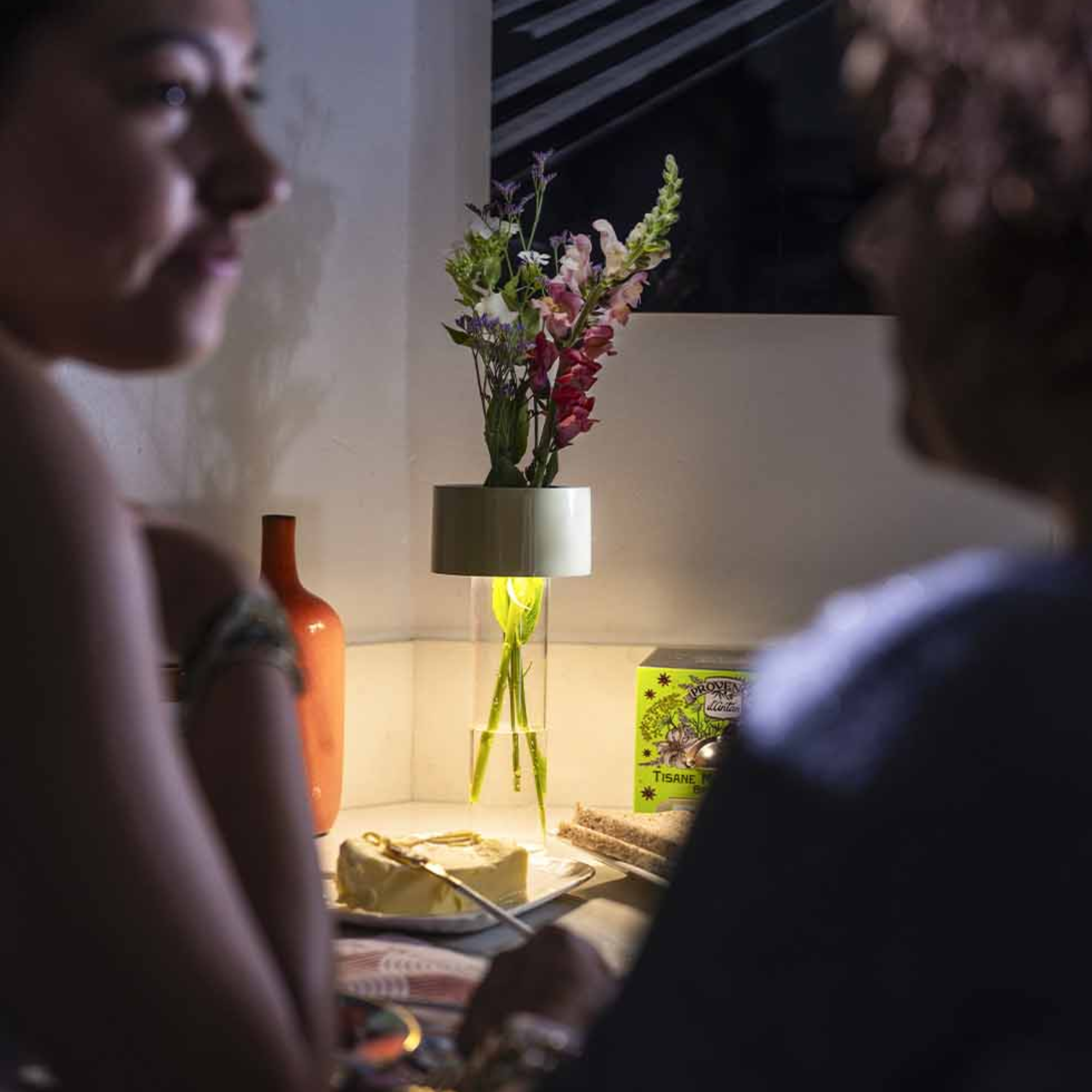 The white Fleur Portable Table Lamp from Foscarini in a living room on top of a table holding flowers.