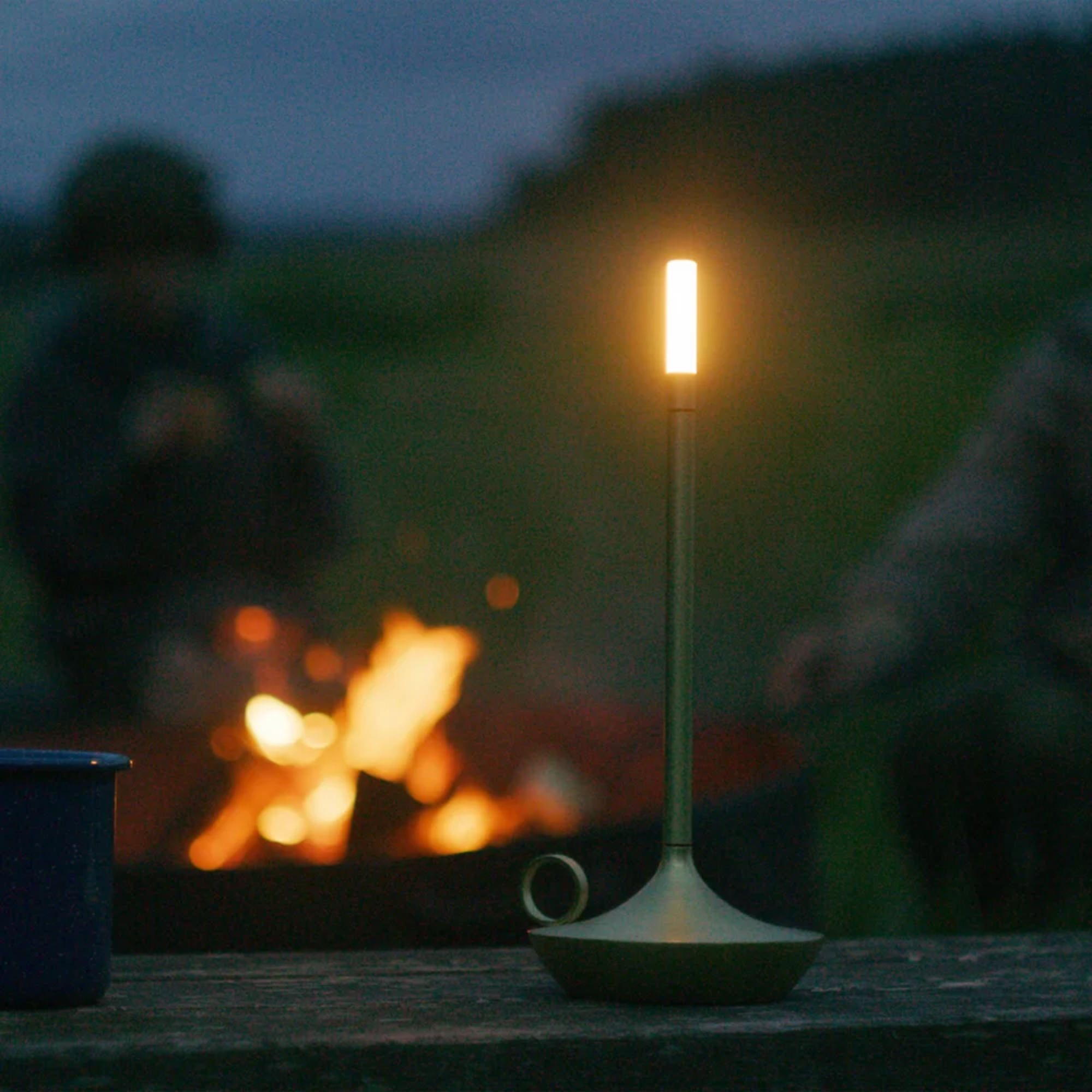 The brass Wick Cordless Lamp from Graypants used while camping, resting on top of a wooden bench. all-groups