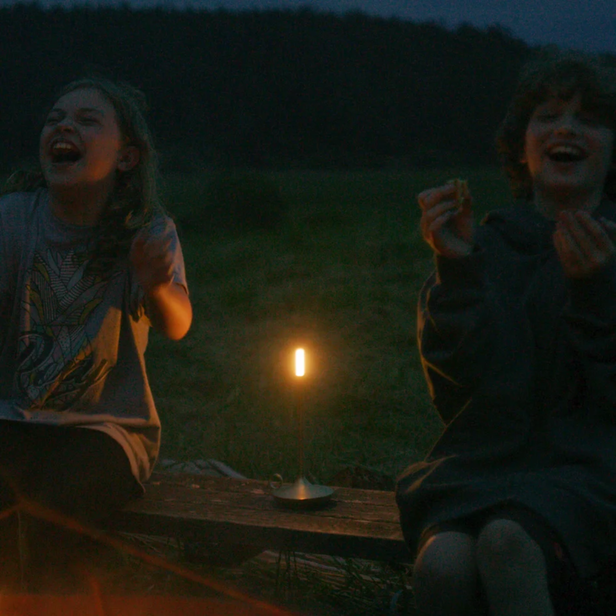 The brass Wick Cordless Lamp from Graypants on a wooden bench between two people eating smores while camping.