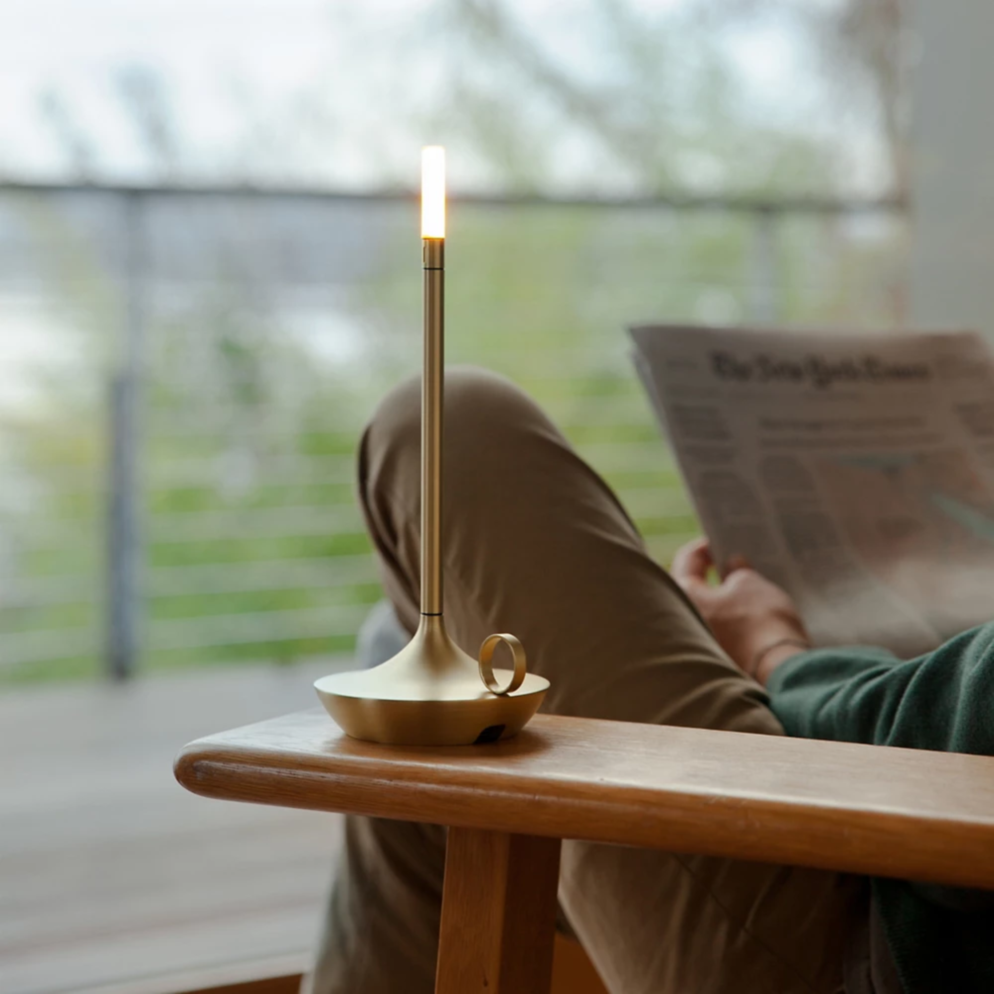 The brass Wick Cordless Lamp from Graypants on the arm of a lounge chair on an outdoor patio.
