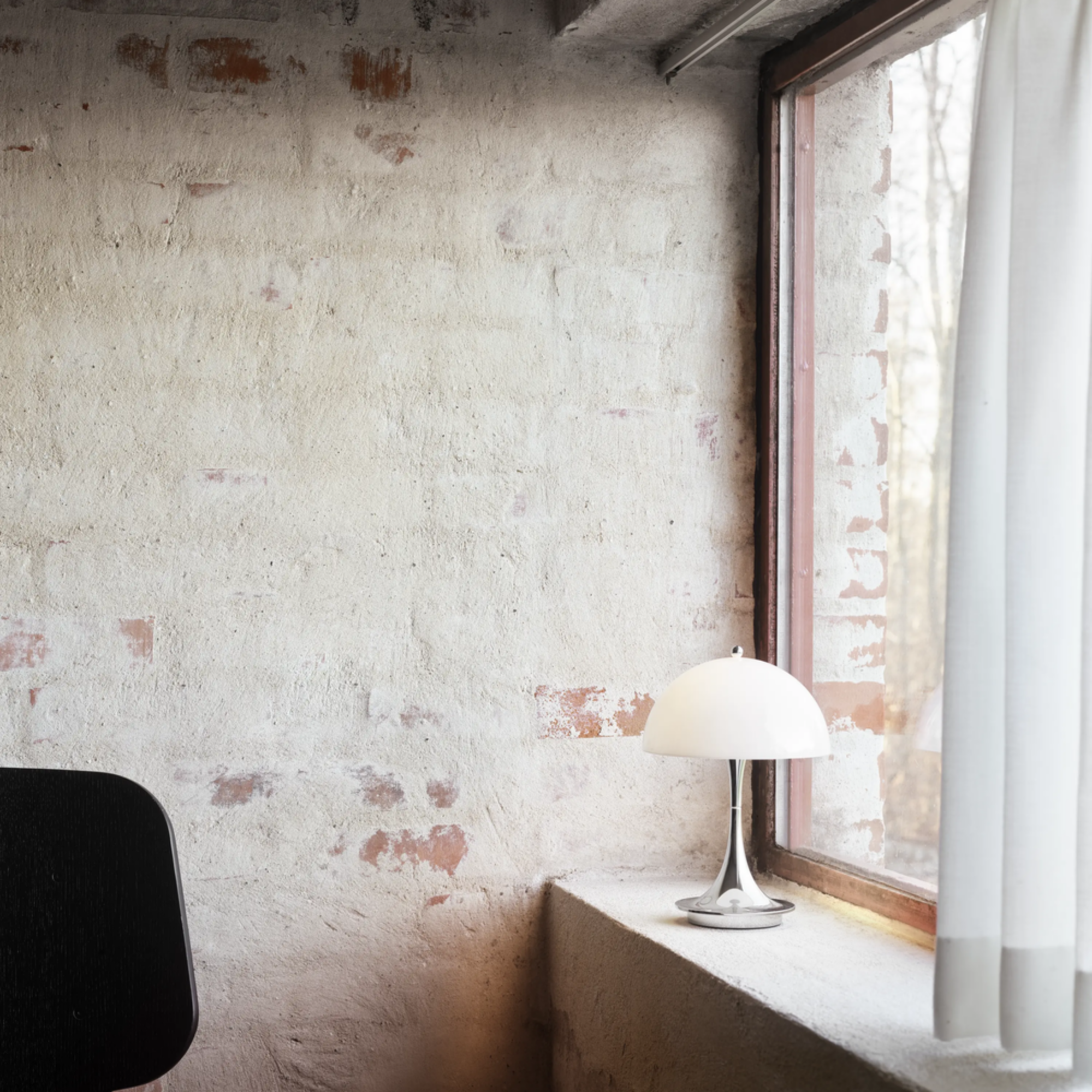 The grey opal Panthella 160 Portable Lamp from Louis Poulsen in a living space beside the window.