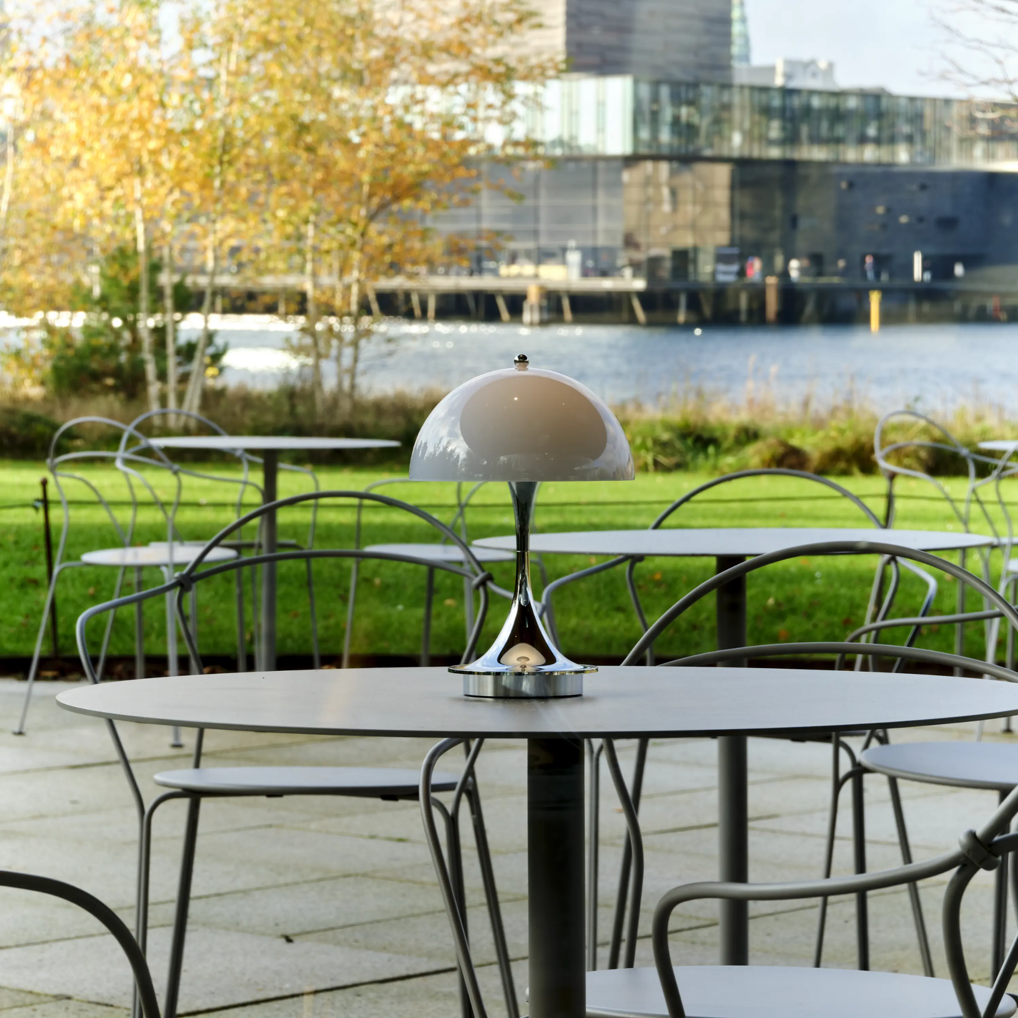 The grey opal Panthella 160 Portable Lamp from Louis Poulsen in an outdoor terrace on top of an cafe table with a view.