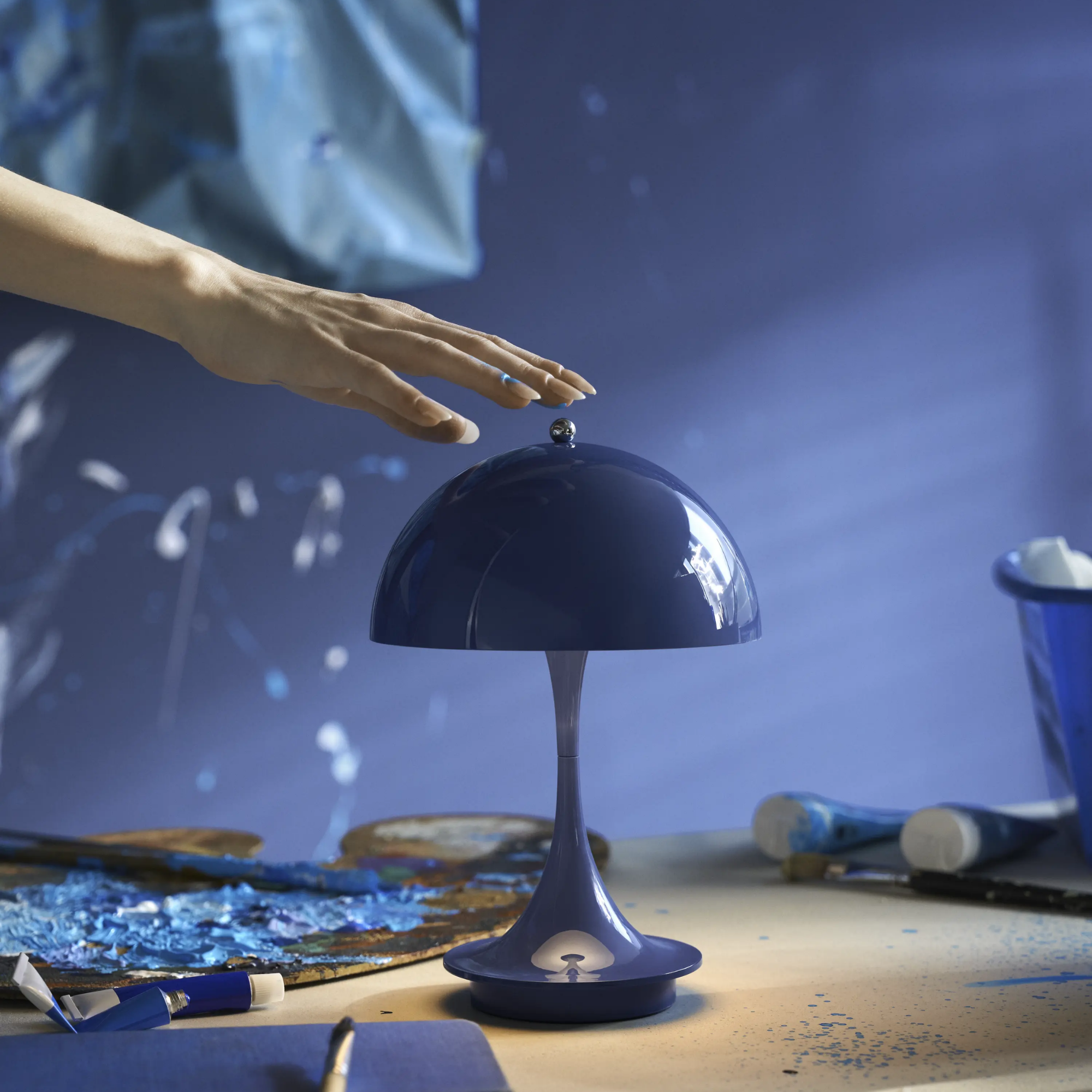 The opaque indigo Panthella 160 Portable Lamp from Louis Poulsen in a living room with art supplies.