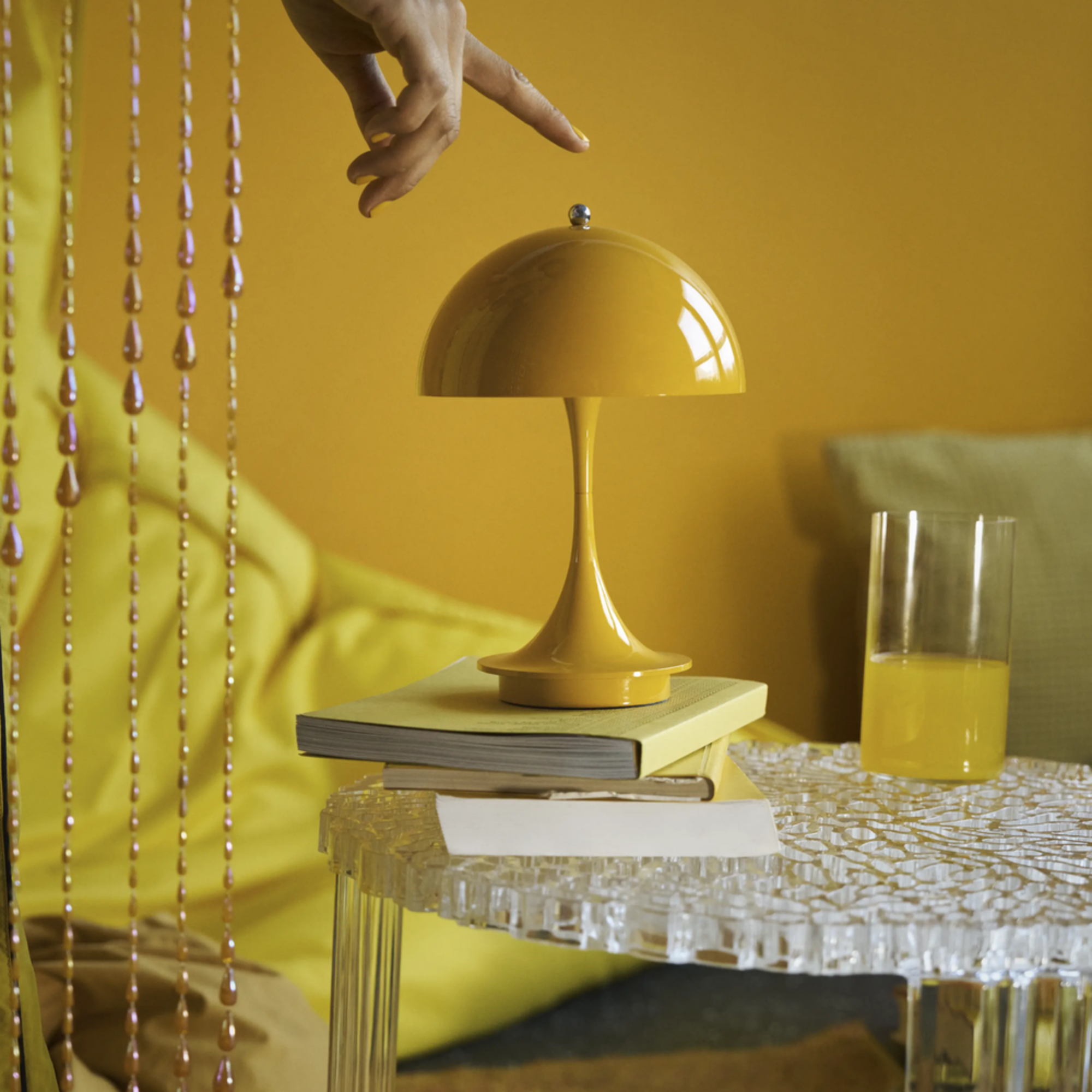 The opaque yellow Panthella 160 Portable Lamp from Louis Poulsen in a lounge on top of a table being used.
