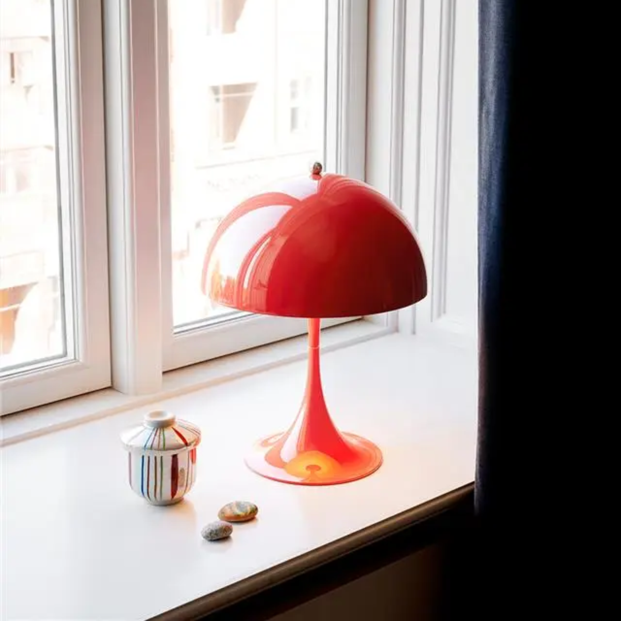 The coral Panthella 250 Portable Lamp from Louis Poulsen in a living room on a windowsill with a couple of trinkets.