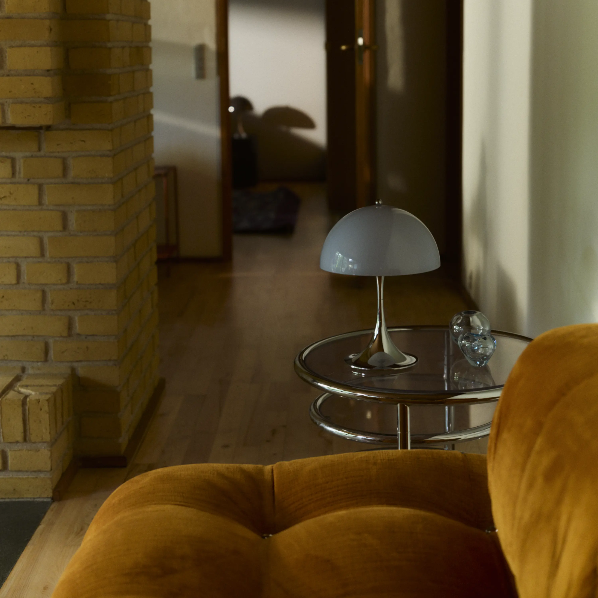 The grey opal Panthella 250 Portable Lamp from Louis Poulsen on a side table beside a sofa in a family area.