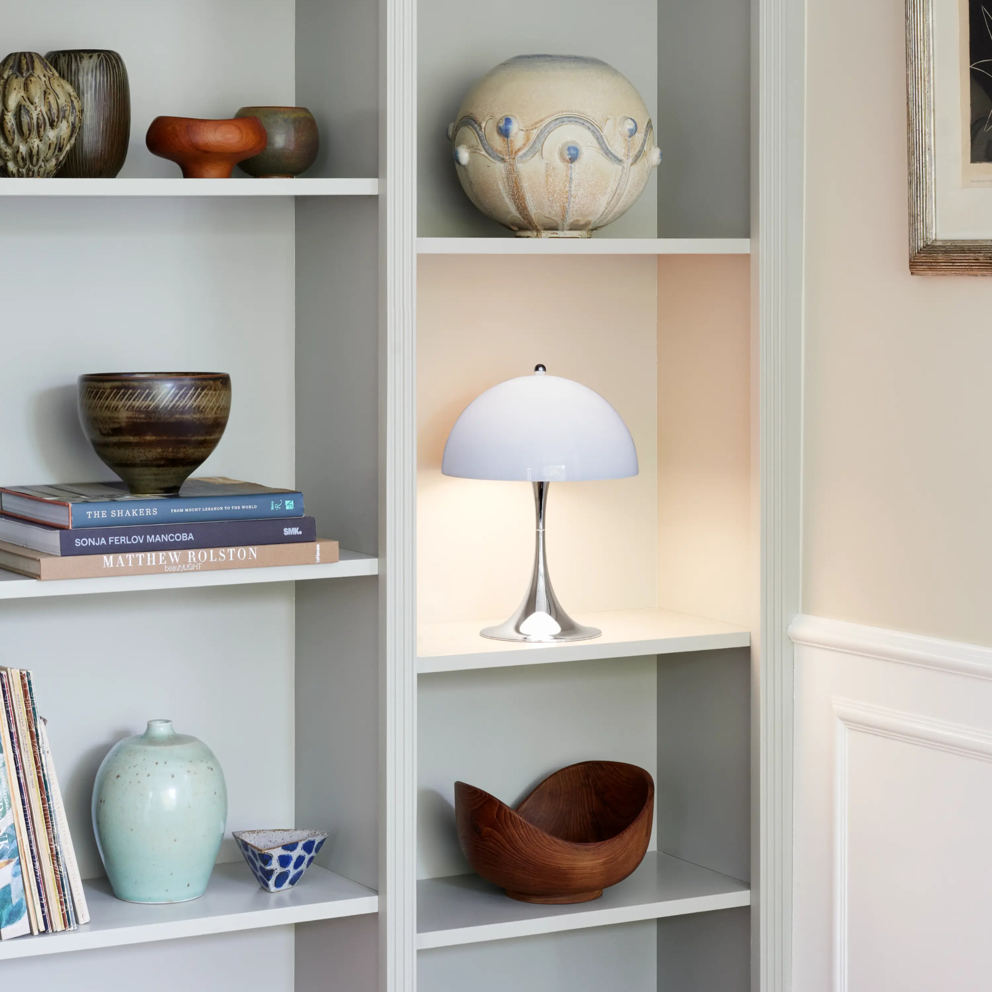The grey opal Panthella 250 Portable Lamp from Louis Poulsen in a living room on a bookshelf with other decor.