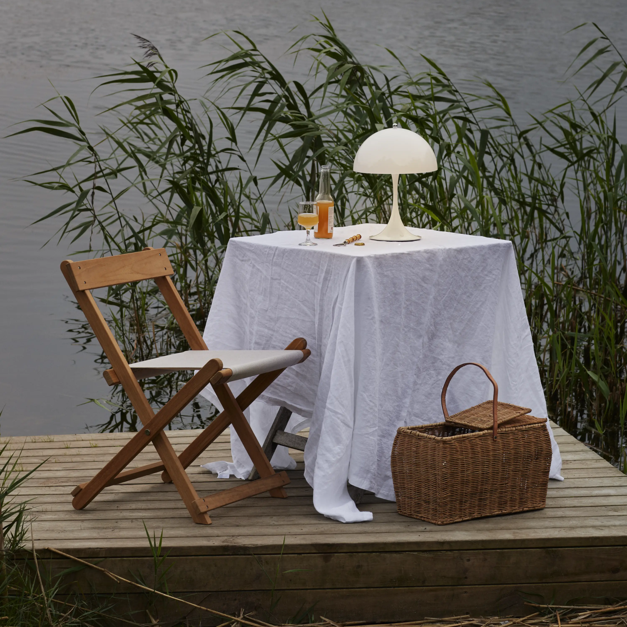 The opal Panthella 250 Portable Lamp from Louis Poulsen in a garden on top of a table with a cloth and a drink.