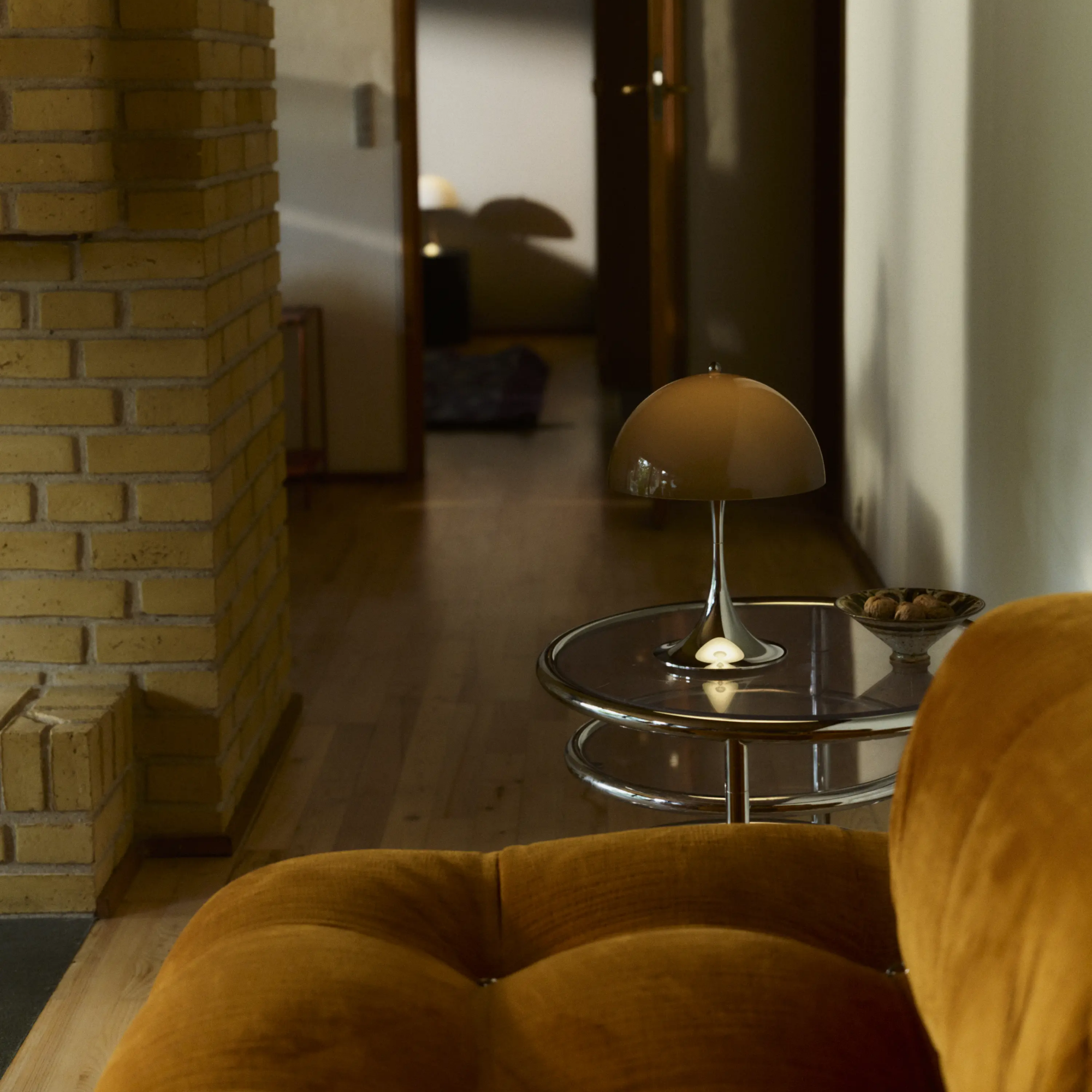 The 13.2 inch brown Panthella Portable Lamp: The Originals from Louis Poulsen in a living room beside a couch on top of an end table.