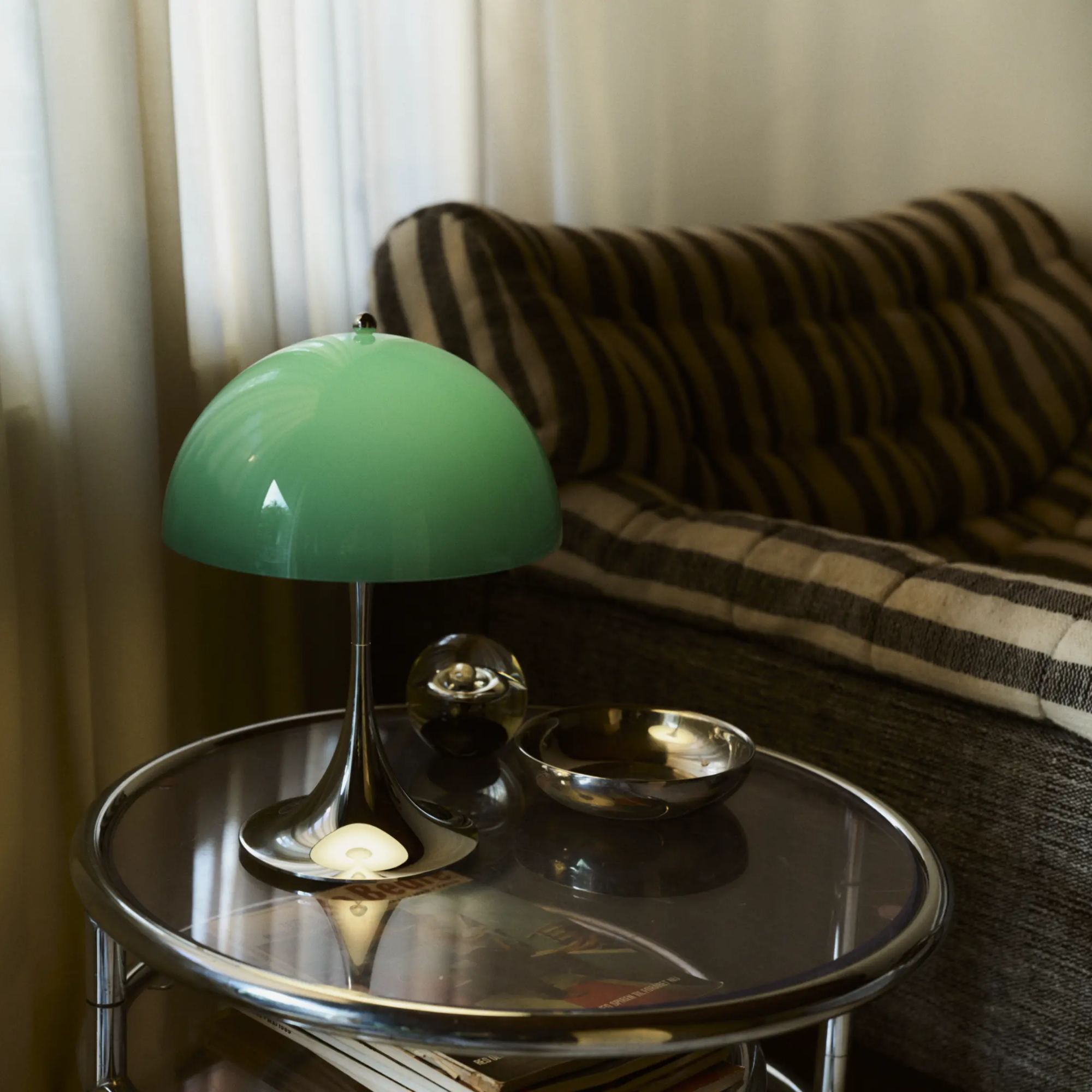 The 13.2 inch green Panthella Portable Lamp: The Originals from Louis Poulsen in a living space on a glass table beside a sofa.
