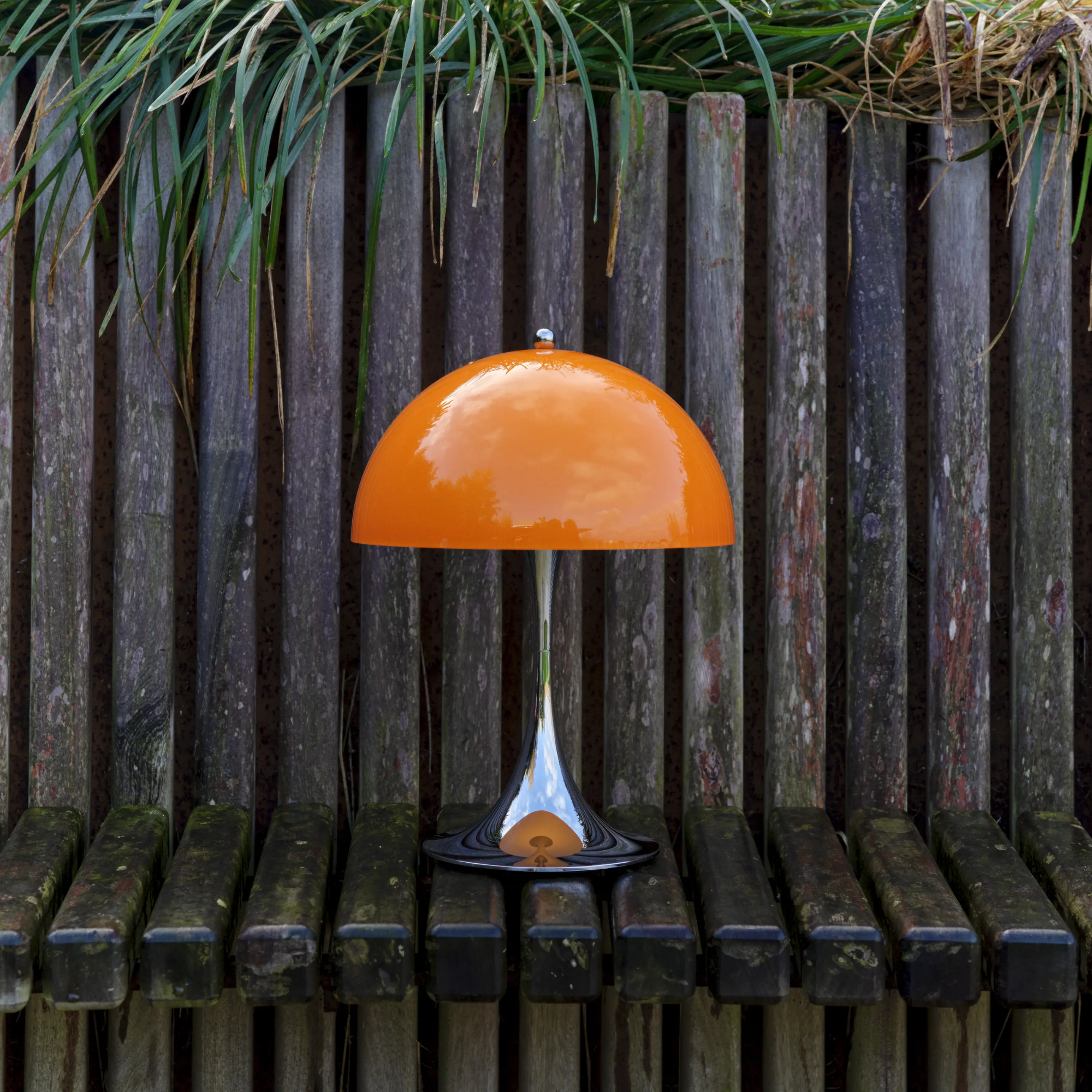 The 13.2 inch orange Panthella Portable Lamp: The Originals from Louis Poulsen in a garden on a wooden bench beside green grass.