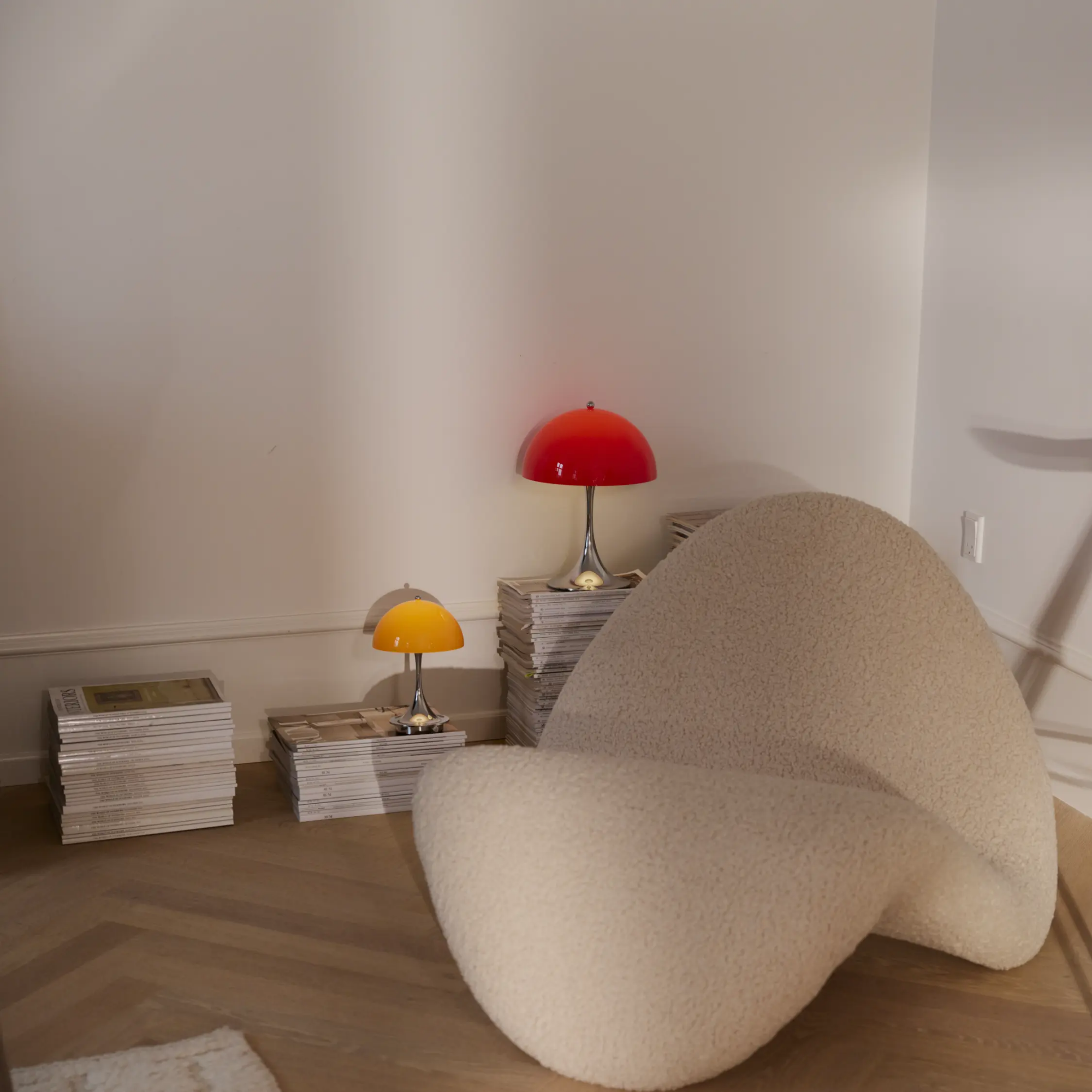 The 9.5 inch orange Panthella Portable Lamp: The Originals from Louis Poulsen in a lounge beside a chair and reading materials.