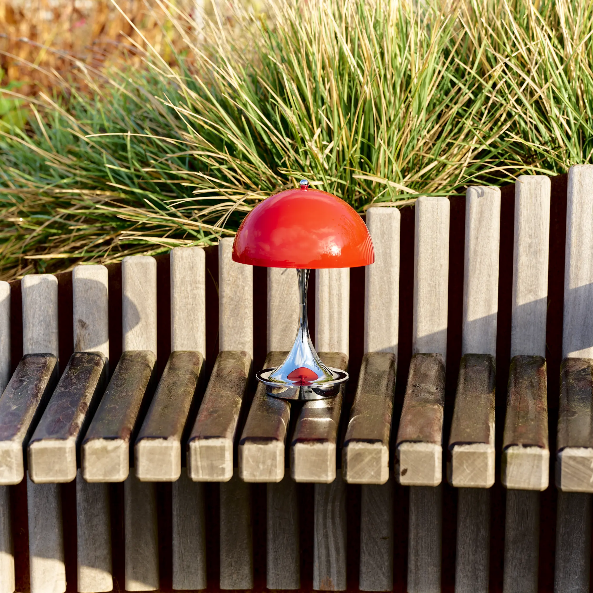 The 9.5 inch red Panthella Portable Lamp: The Originals from Louis Poulsen in a garden beside green plants.