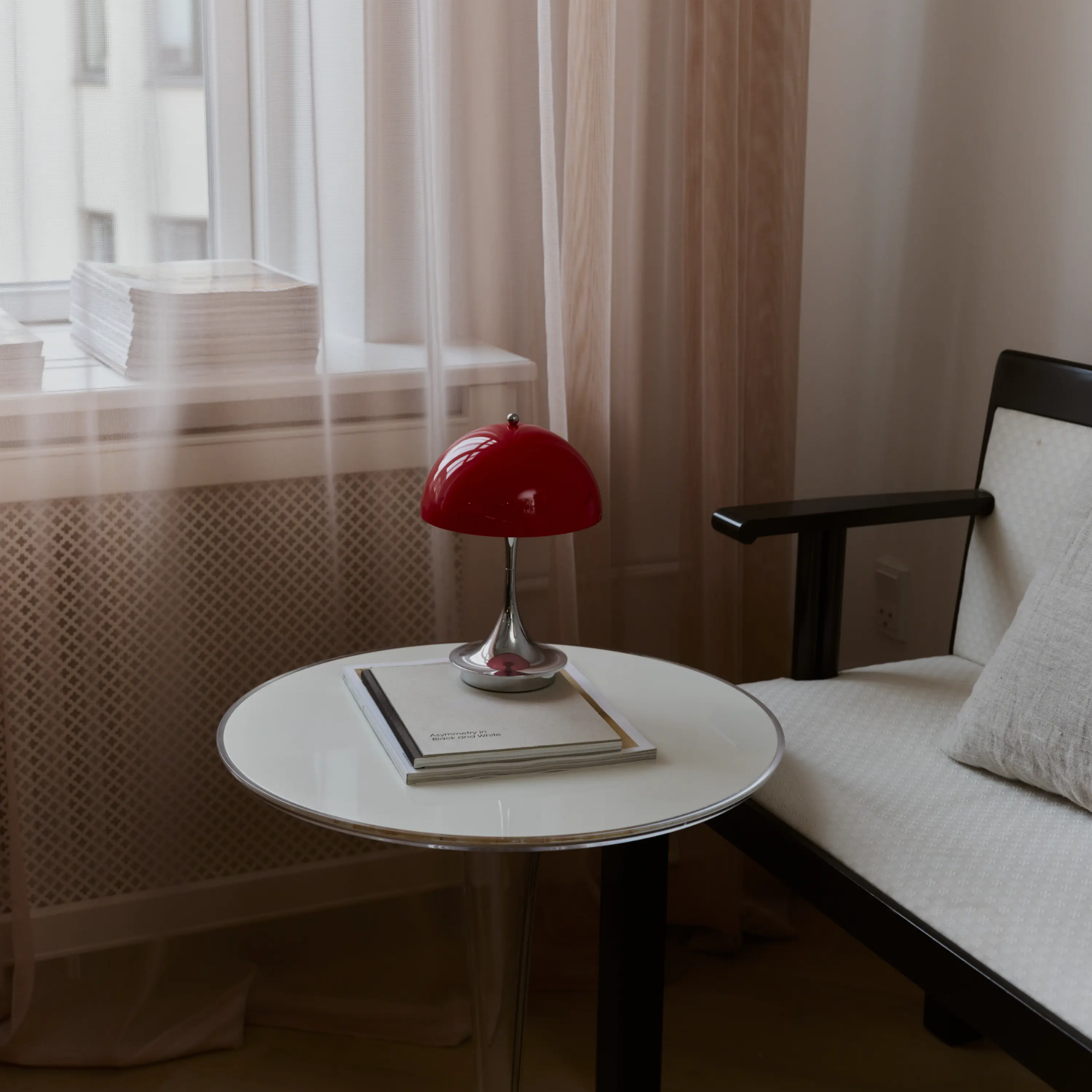 The 9.5 inch red Panthella Portable Lamp: The Originals from Louis Poulsen in a living space next to a sofa on top of a table beside a window.