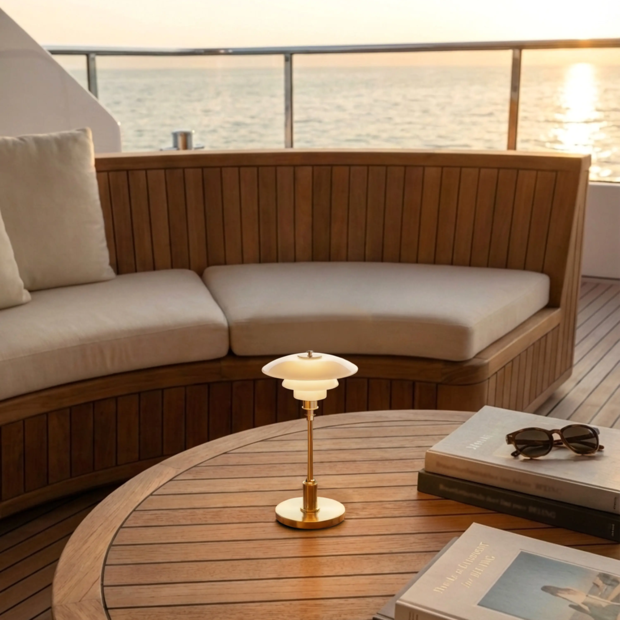 The brass PH 1/1 Portable Lamp from Louis Poulsen in the living space of a boat during sunset on the ocean.