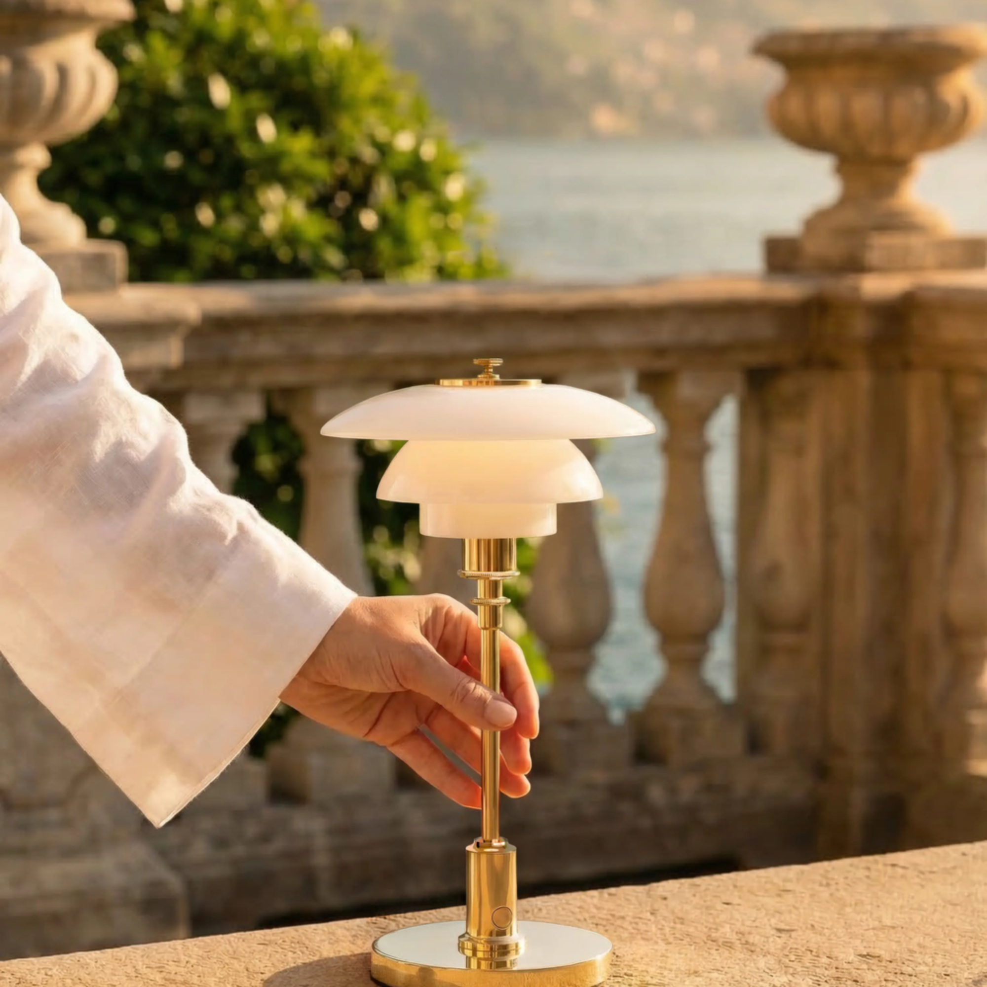 The brass PH 1/1 Portable Lamp from Louis Poulsen used by a model in a home garden with stone detailing.