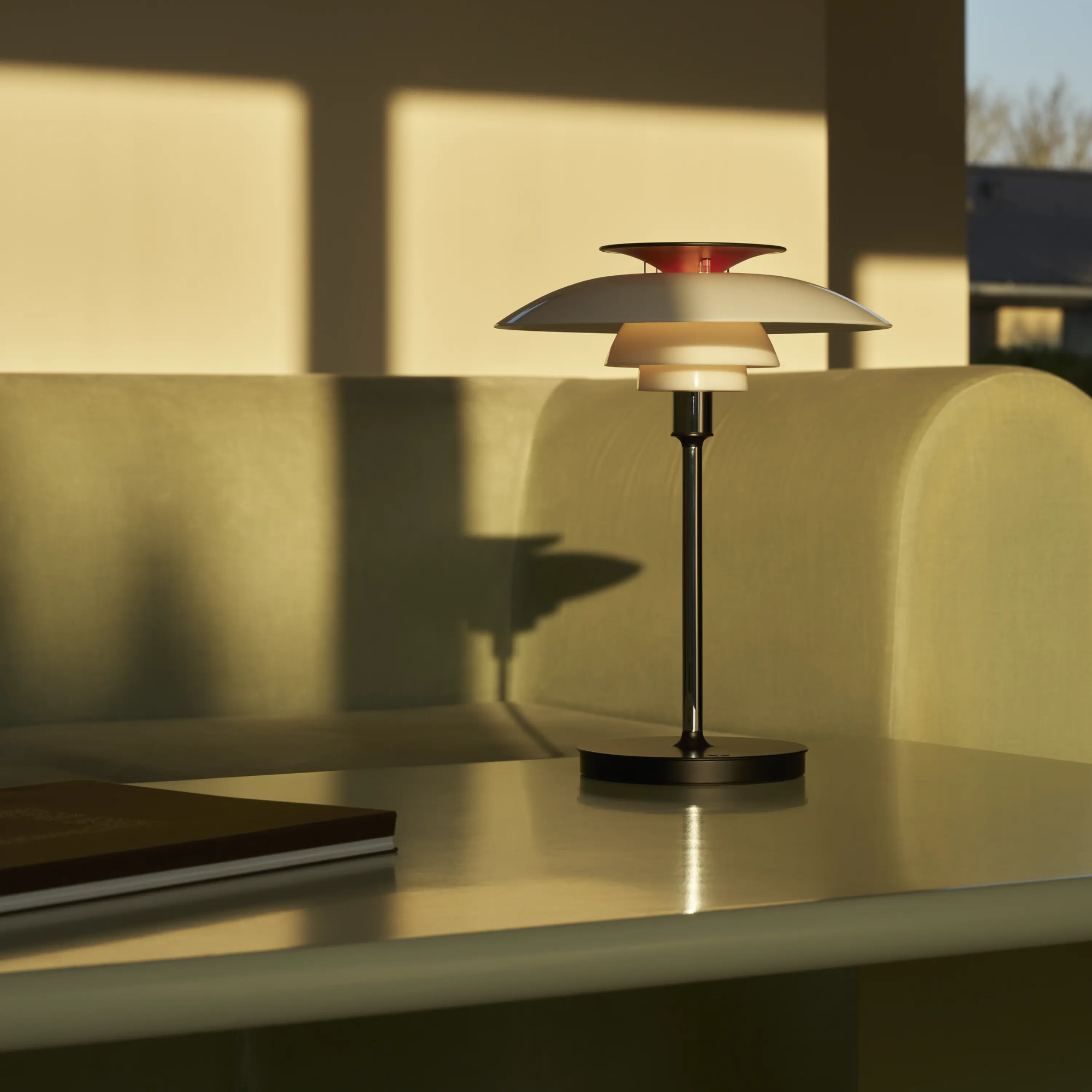 The opal white and high luster chrome plate PH 80 Portable Lamp from Louis Poulsen in a living room on top of a coffee table.