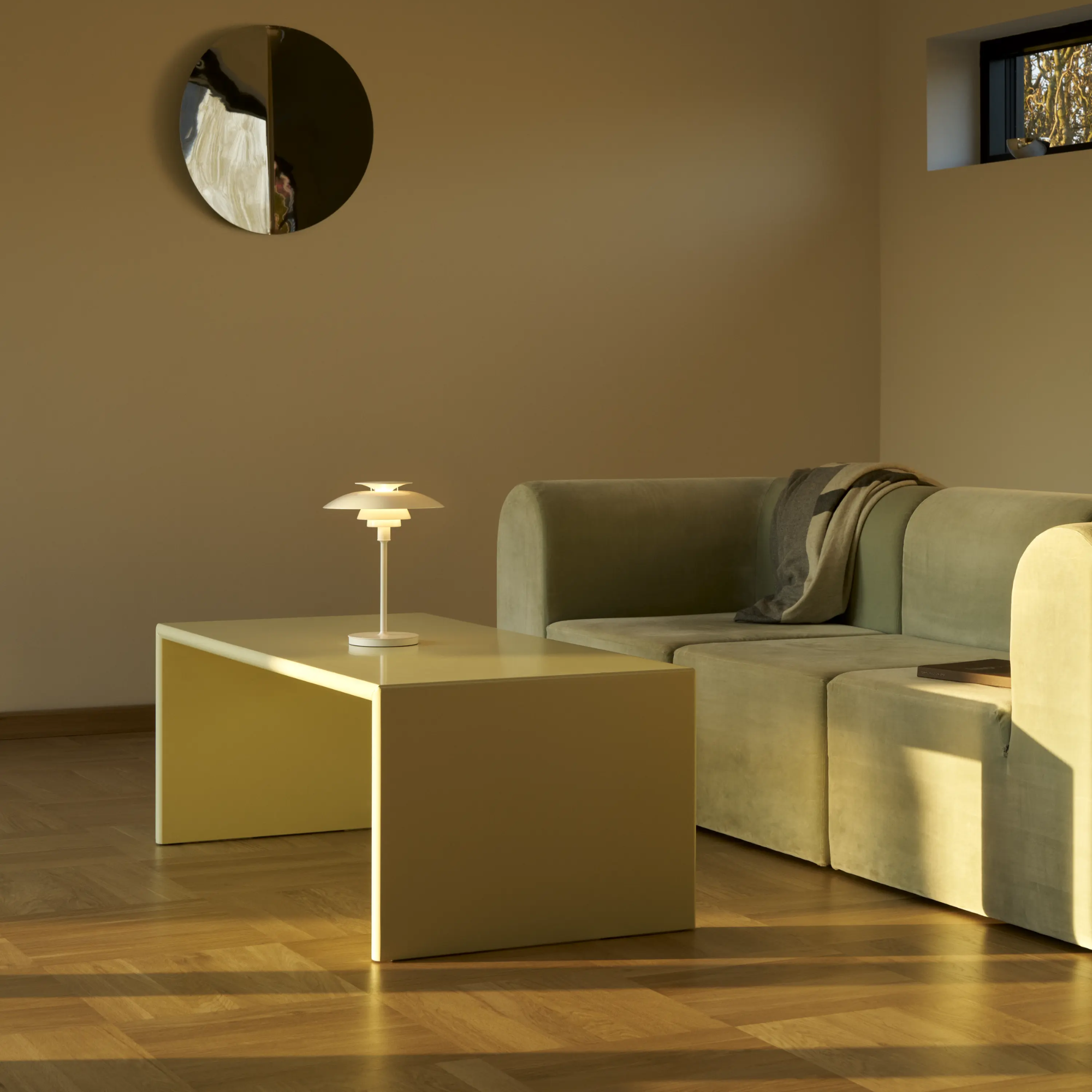 The opal white and white plate PH 80 Portable Lamp from Louis Poulsen in a family area on top of a table in front of a sofa.
