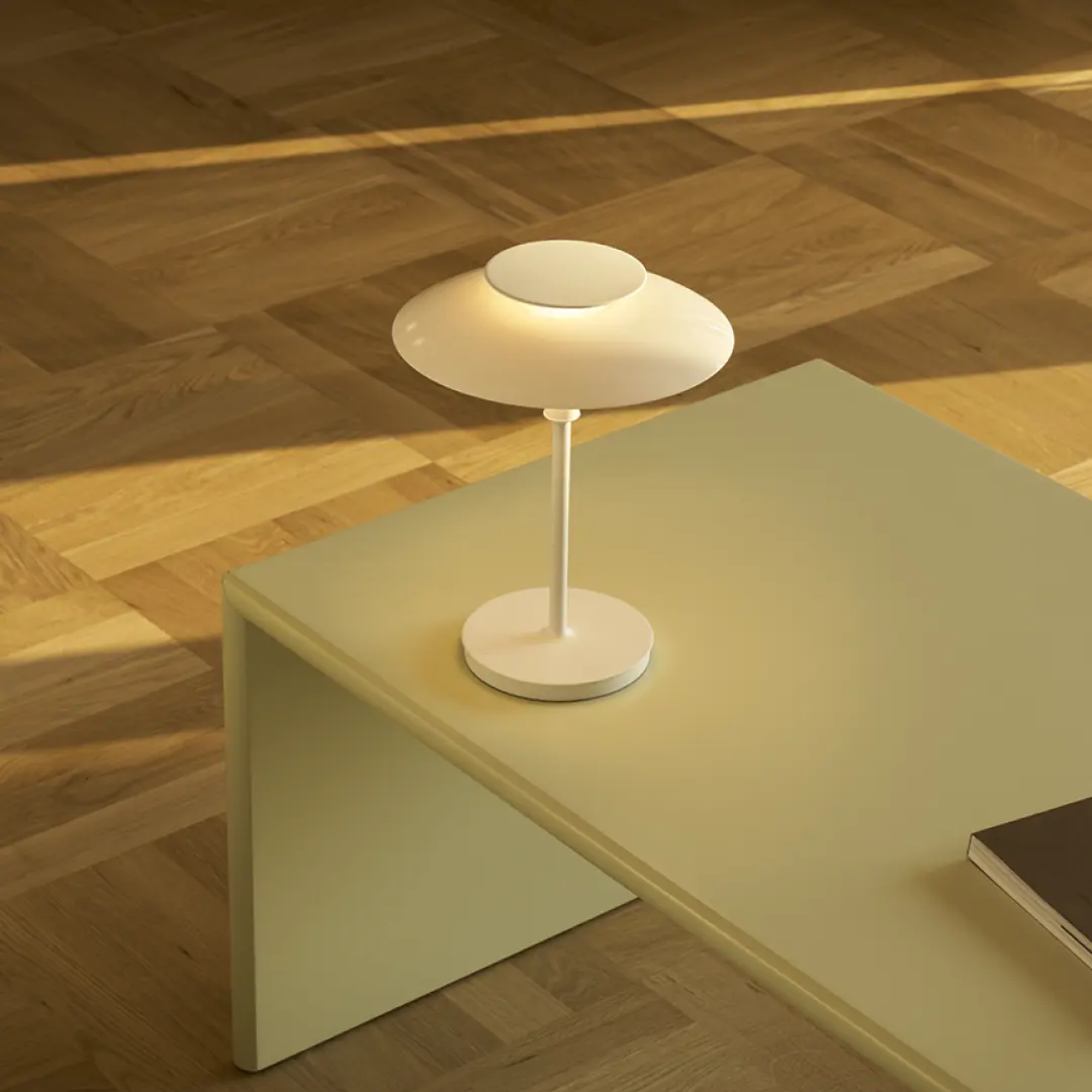 The opal white and white plate PH 80 Portable Lamp from Louis Poulsen in a home office on top of a coffee table.