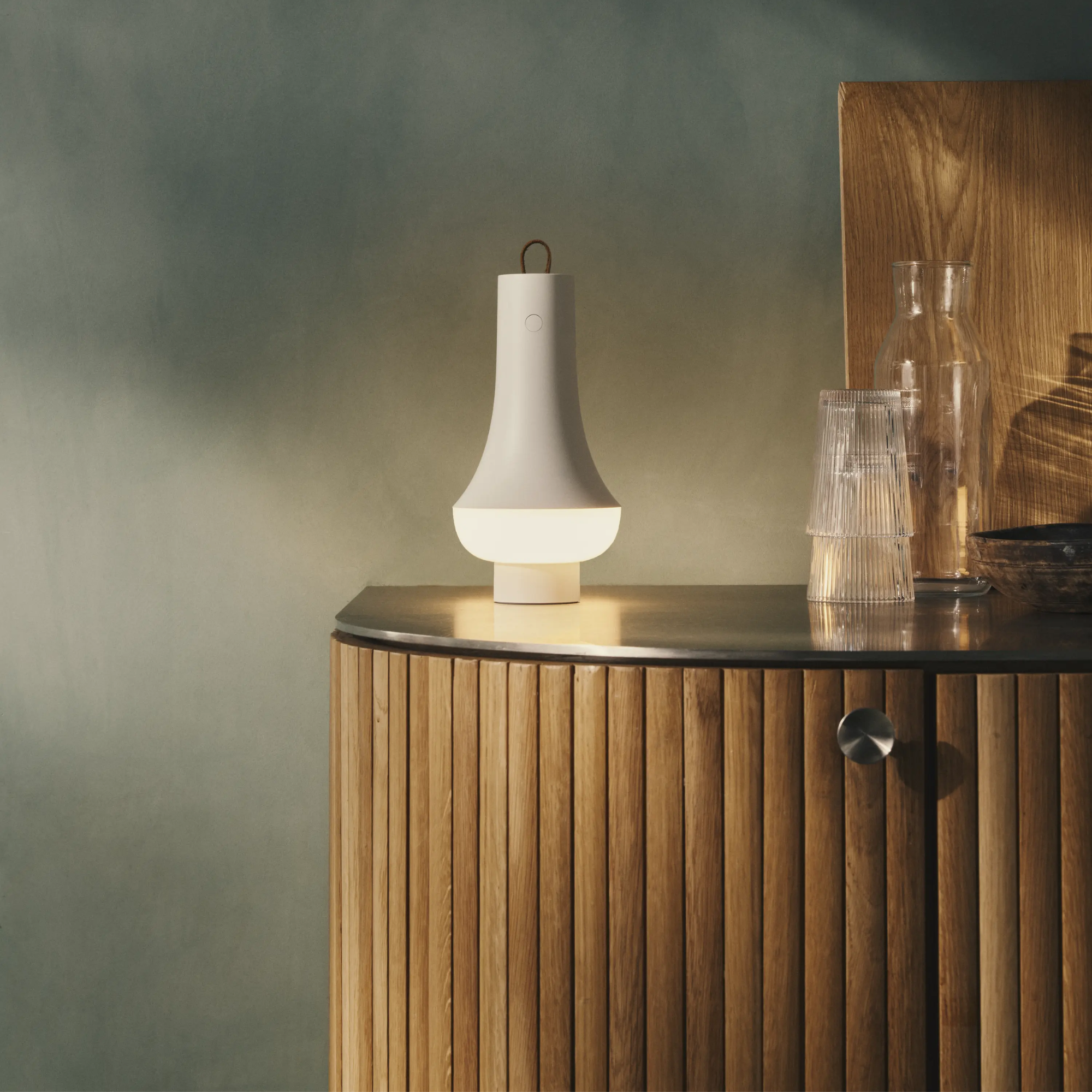 The white Tomoshi Portable Lamp from Louis Poulsen in a bar table beside a glass drink set.