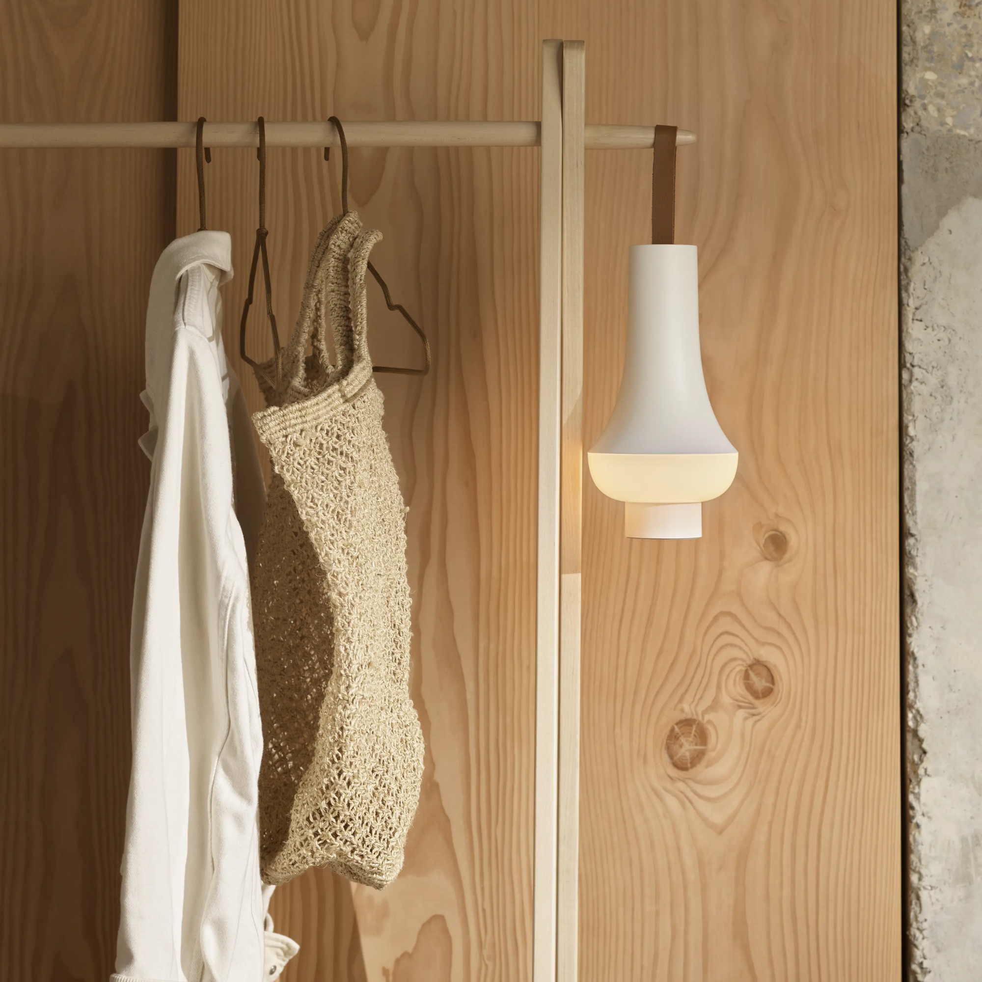 The white Tomoshi Portable Lamp from Louis Poulsen on a coat hanger in an entryway.
