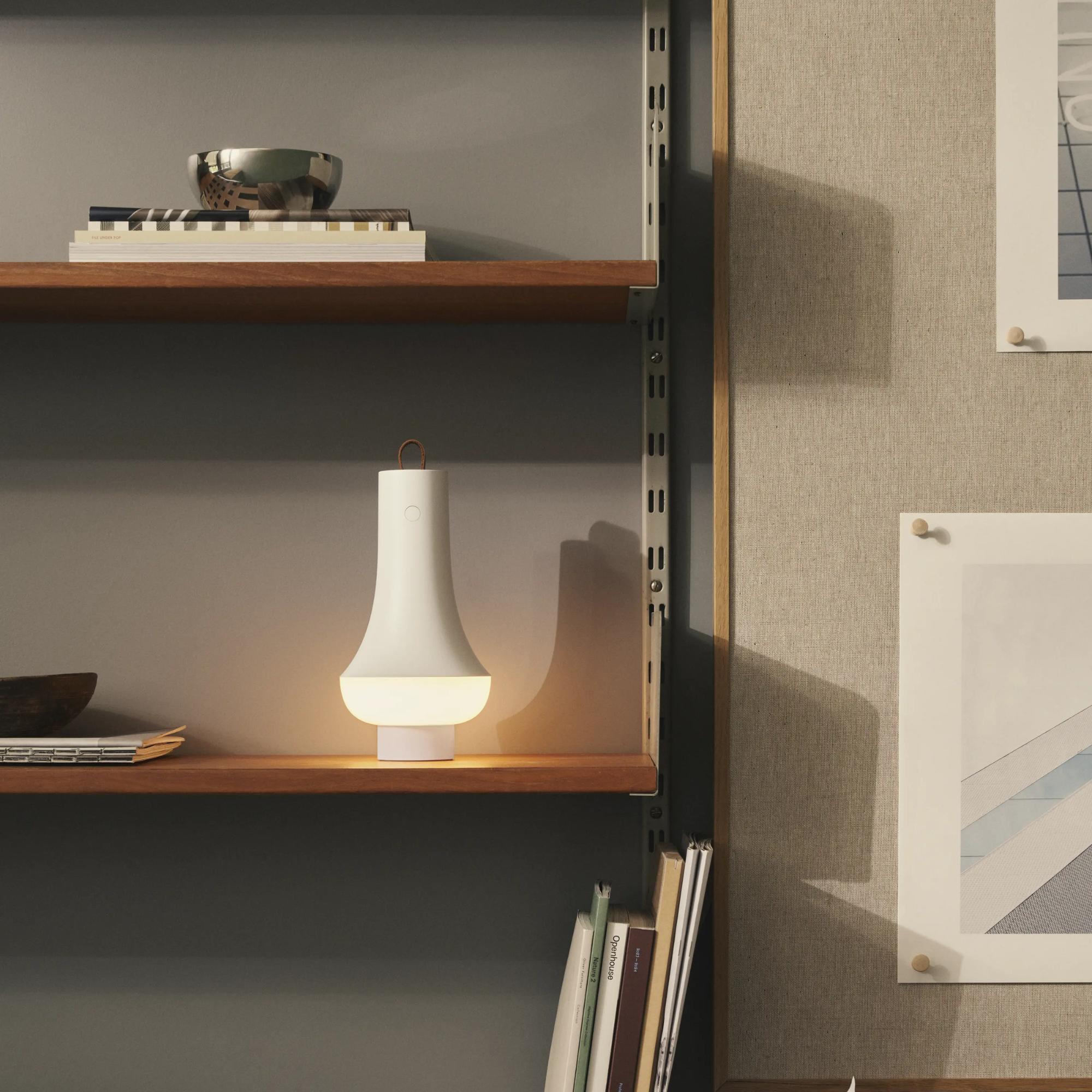 The white Tomoshi Portable Lamp from Louis Poulsen in a home office on a shelf beside other decor.