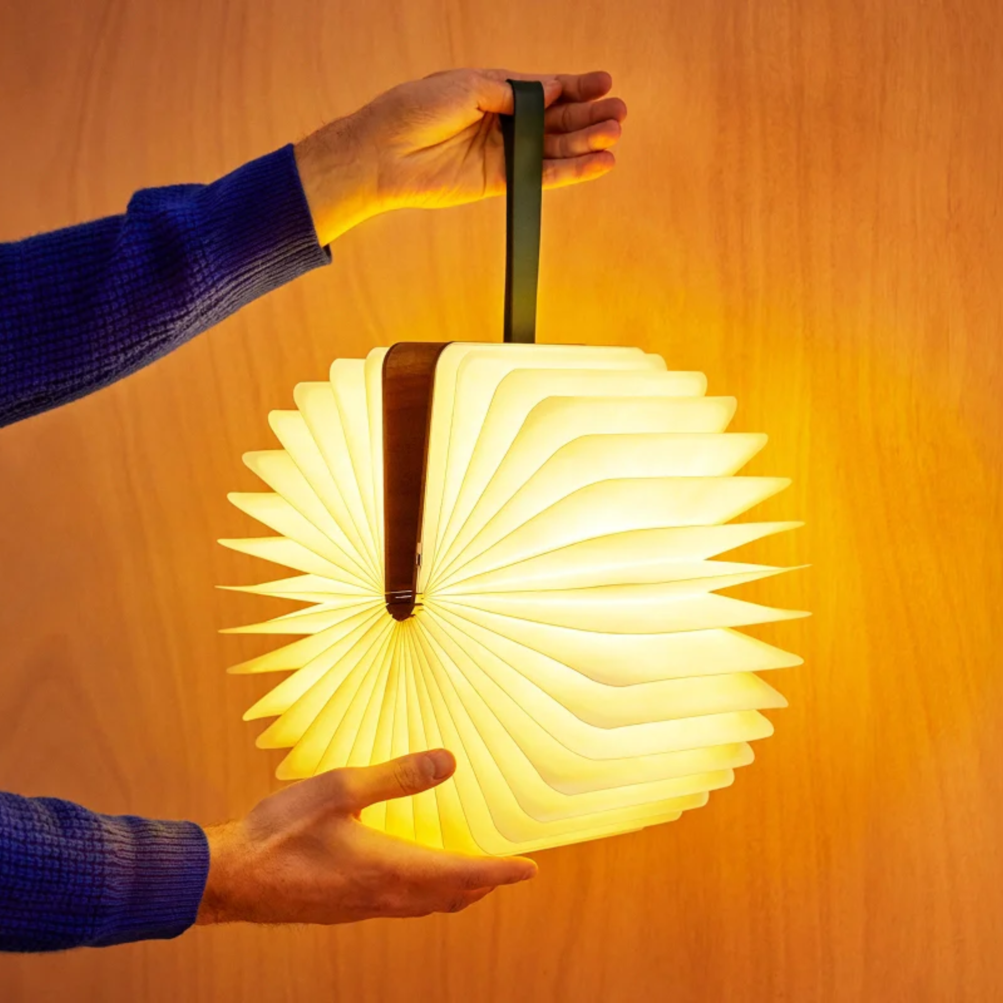 The Lito Classic Wood Cordless Book Lamp from Lumio in a living room held by a model.