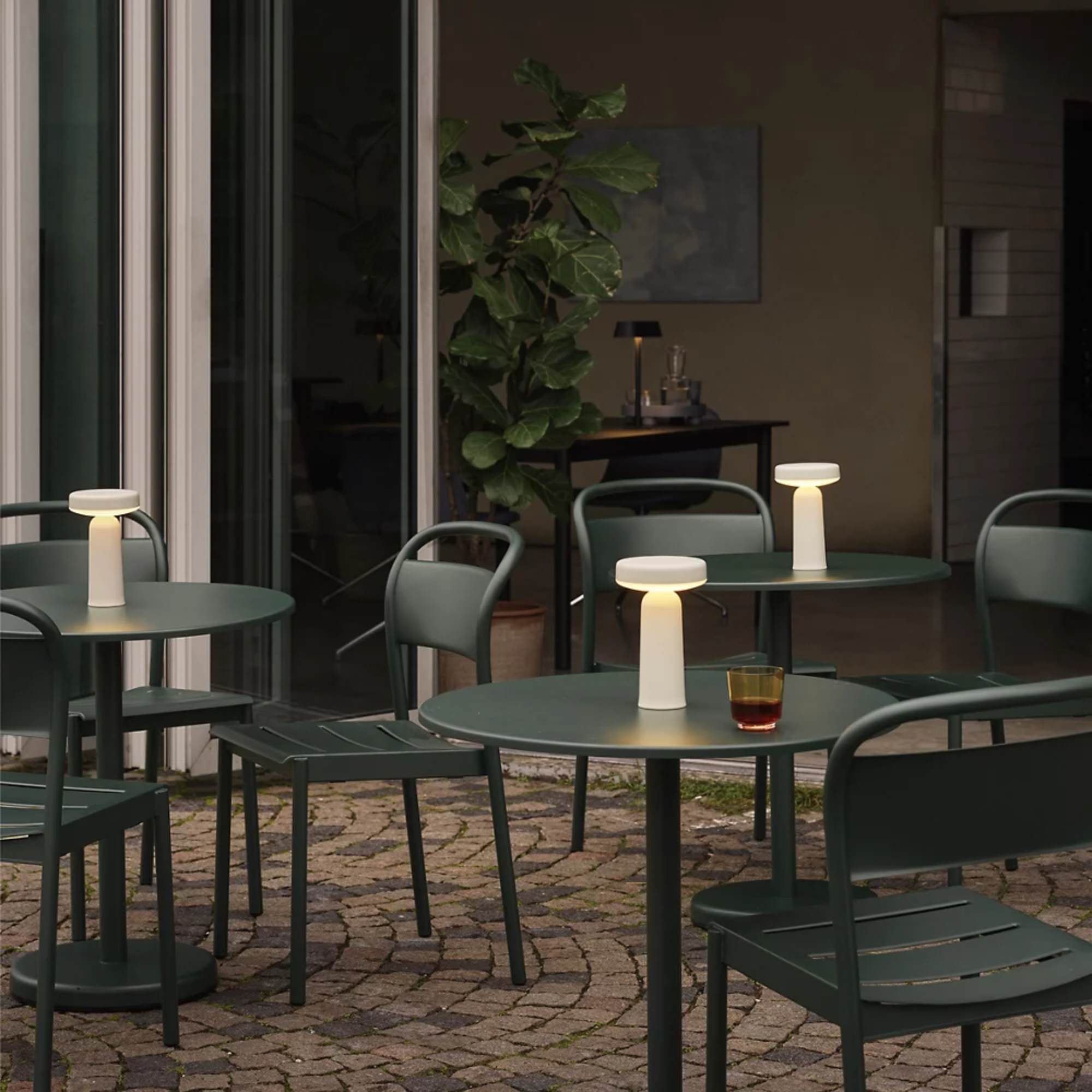 The gray Ease Cordless Lamp from Muuto on top of cafe tables at an outdoor restaurant.