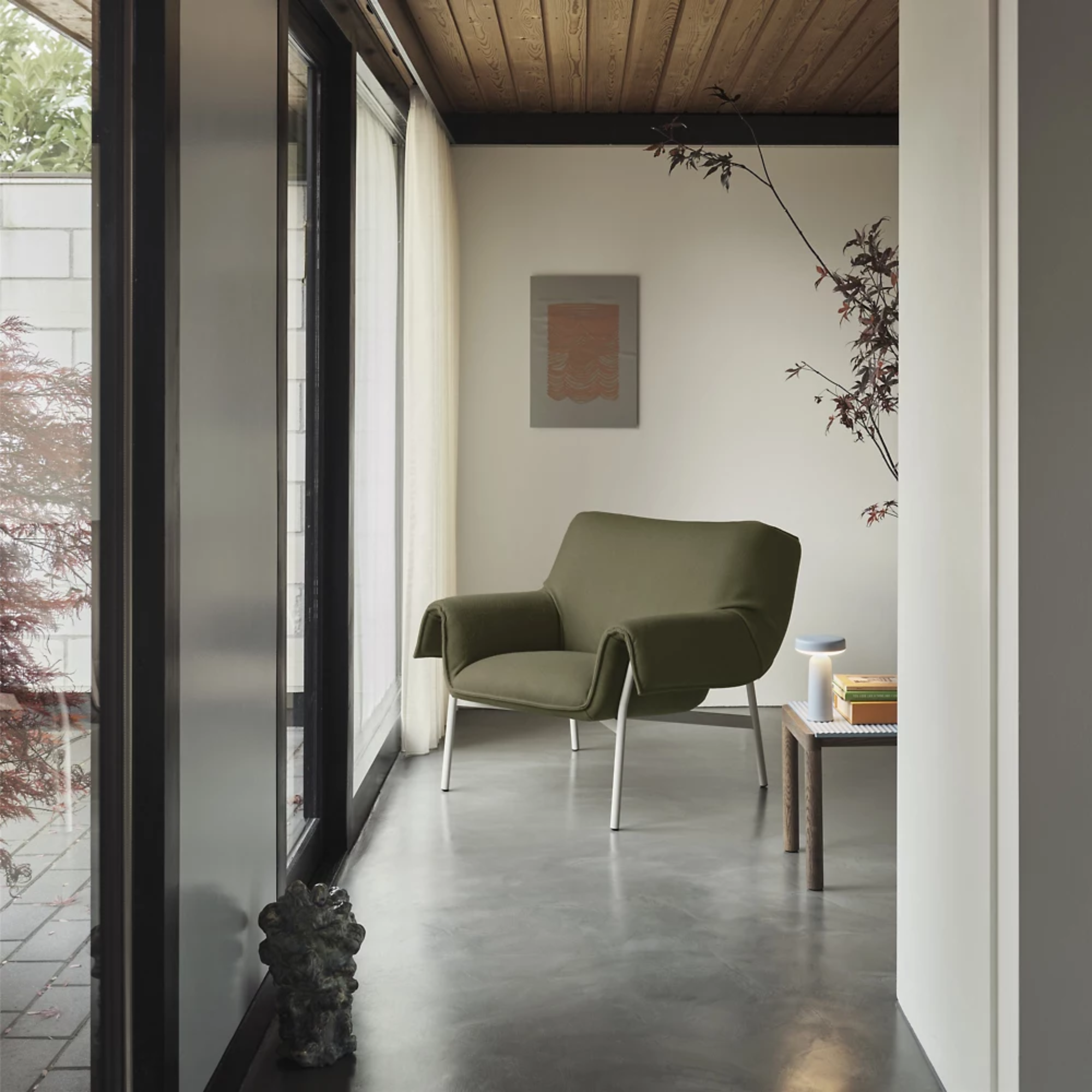 The light blue Ease Cordless Lamp from Muuto in a lounge on top of a table next to a chair.