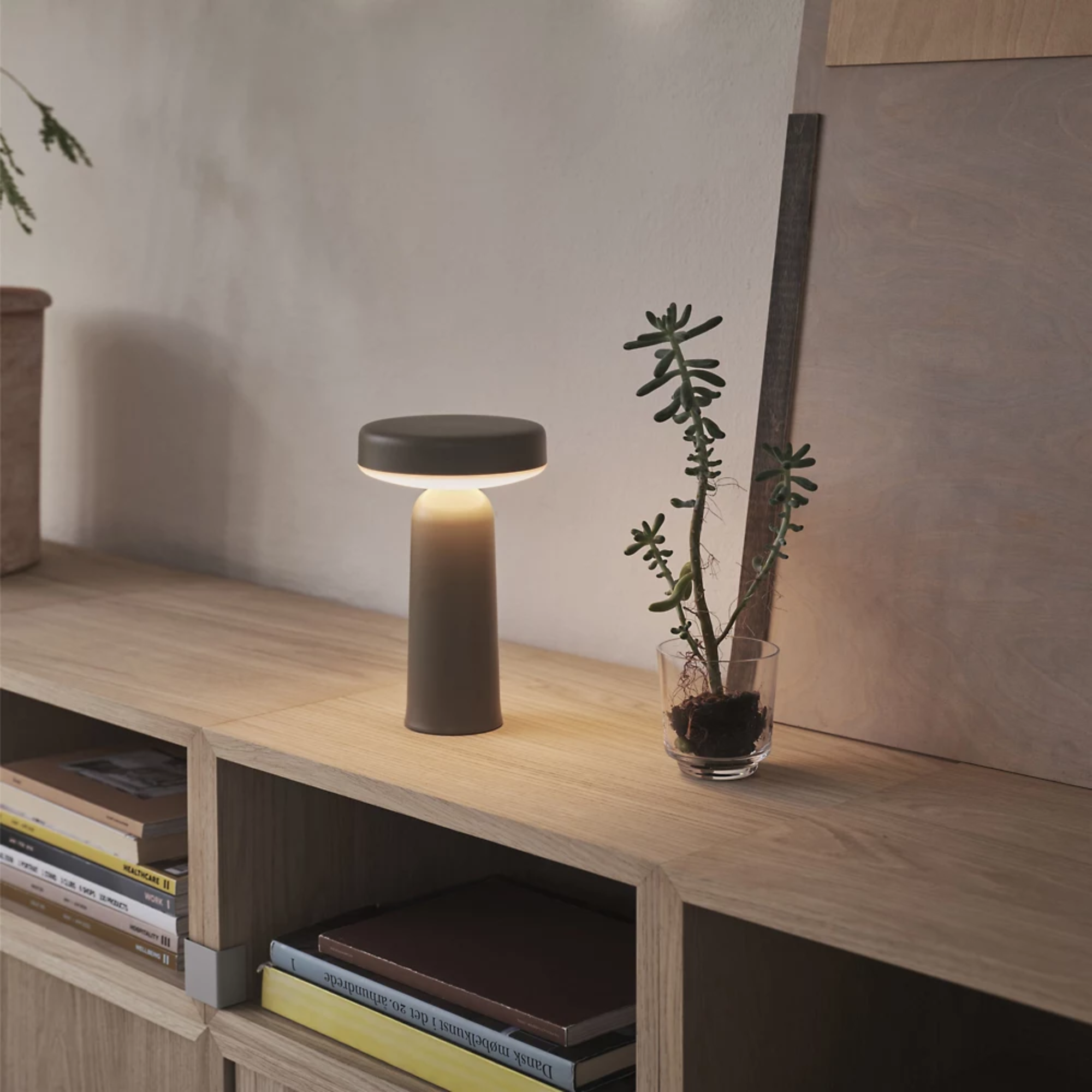 The taupe Ease Cordless Lamp from Muuto in a living space on top of a wooden table.