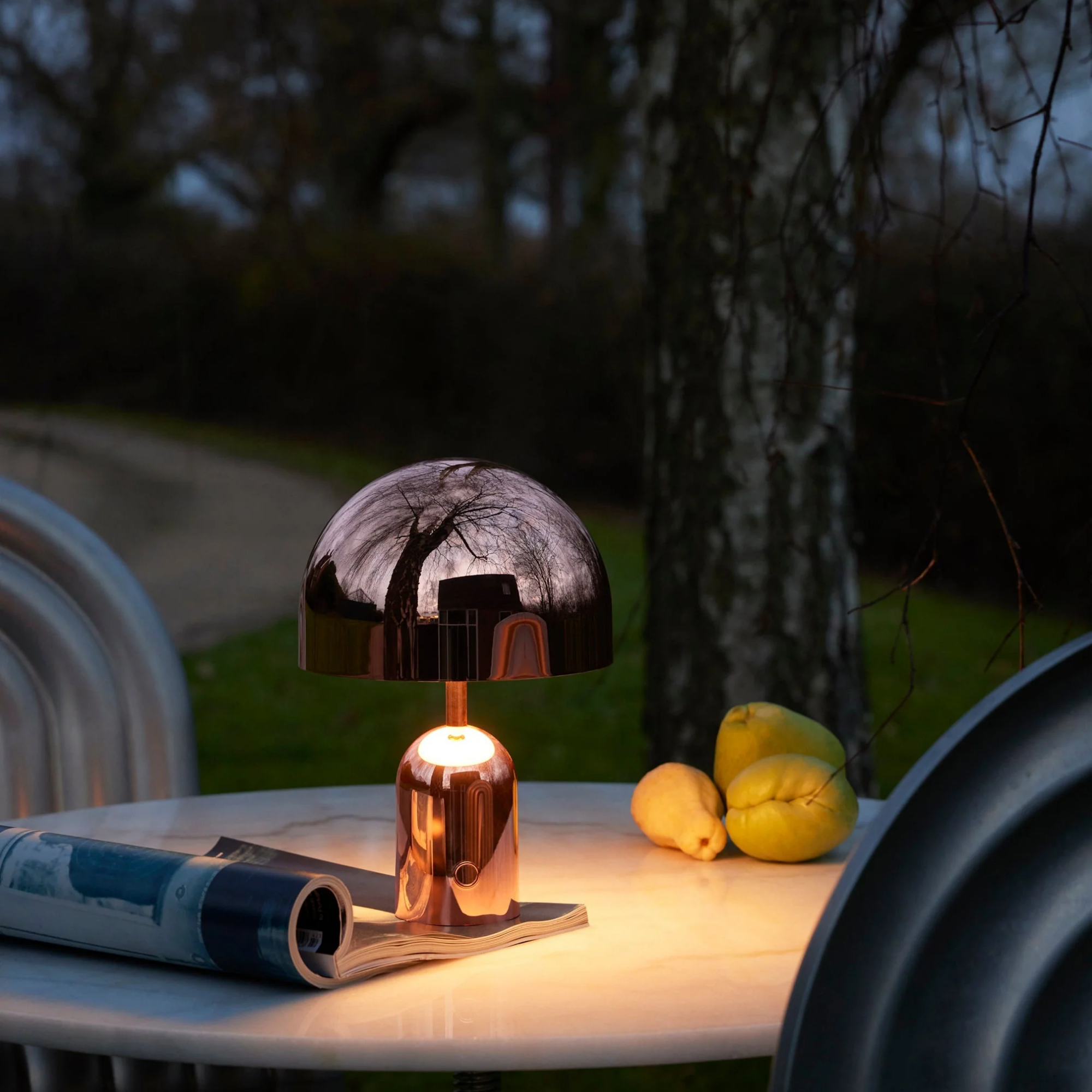 The copper Bell Cordless Lamp from Tom Dixon used on an outdoor marble dining table.