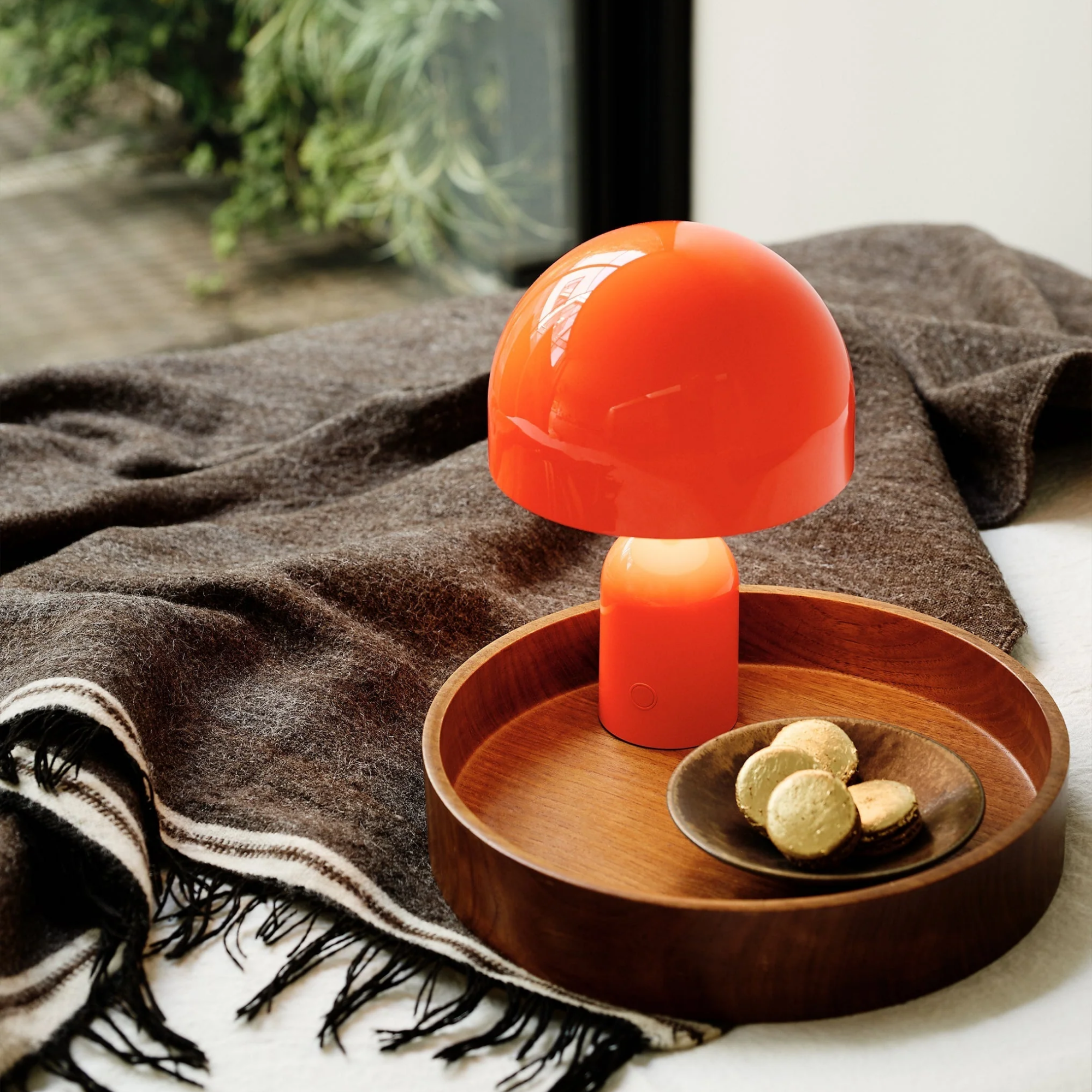 The fluoro Bell Cordless Lamp from Tom Dixon in a bedroom on top of a tray and blanket.