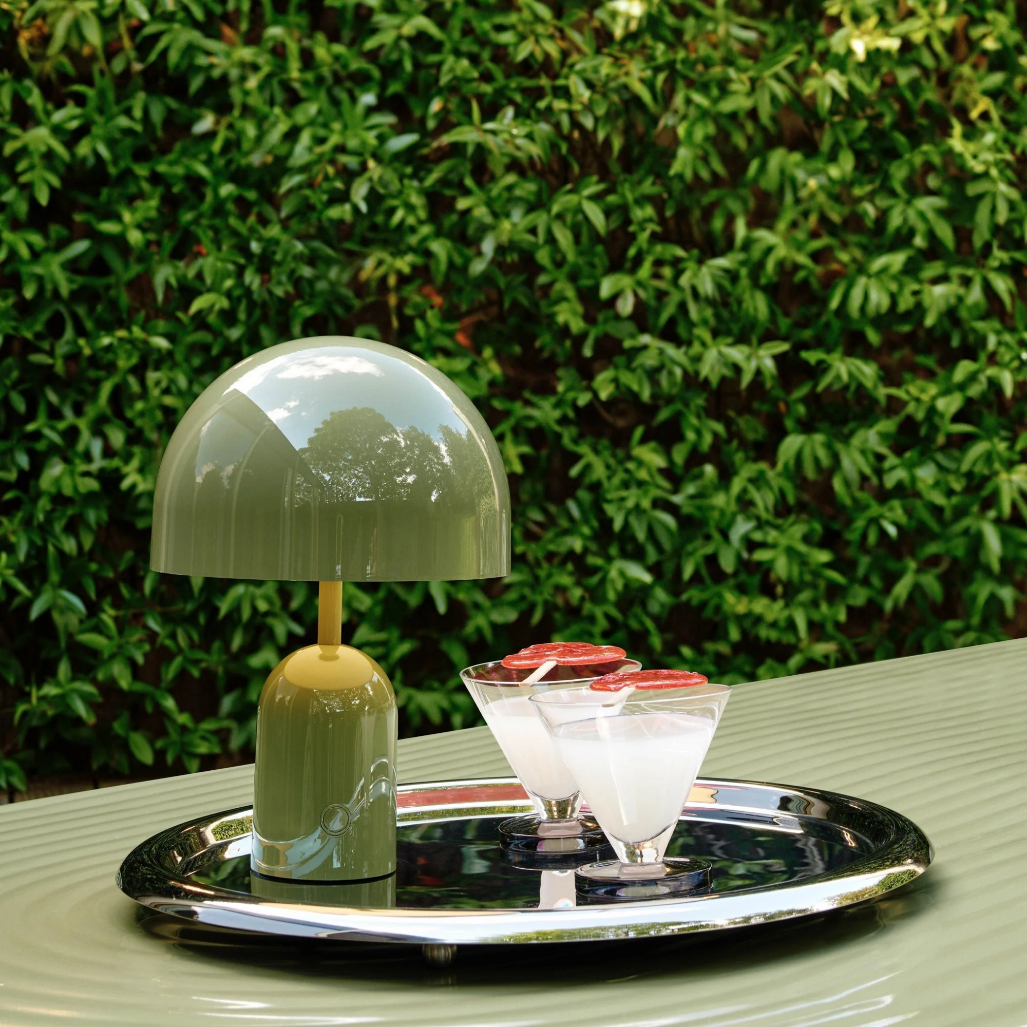 The moss Bell Cordless Lamp from Tom Dixon shown next to a couple drinks in an outdoor bar.