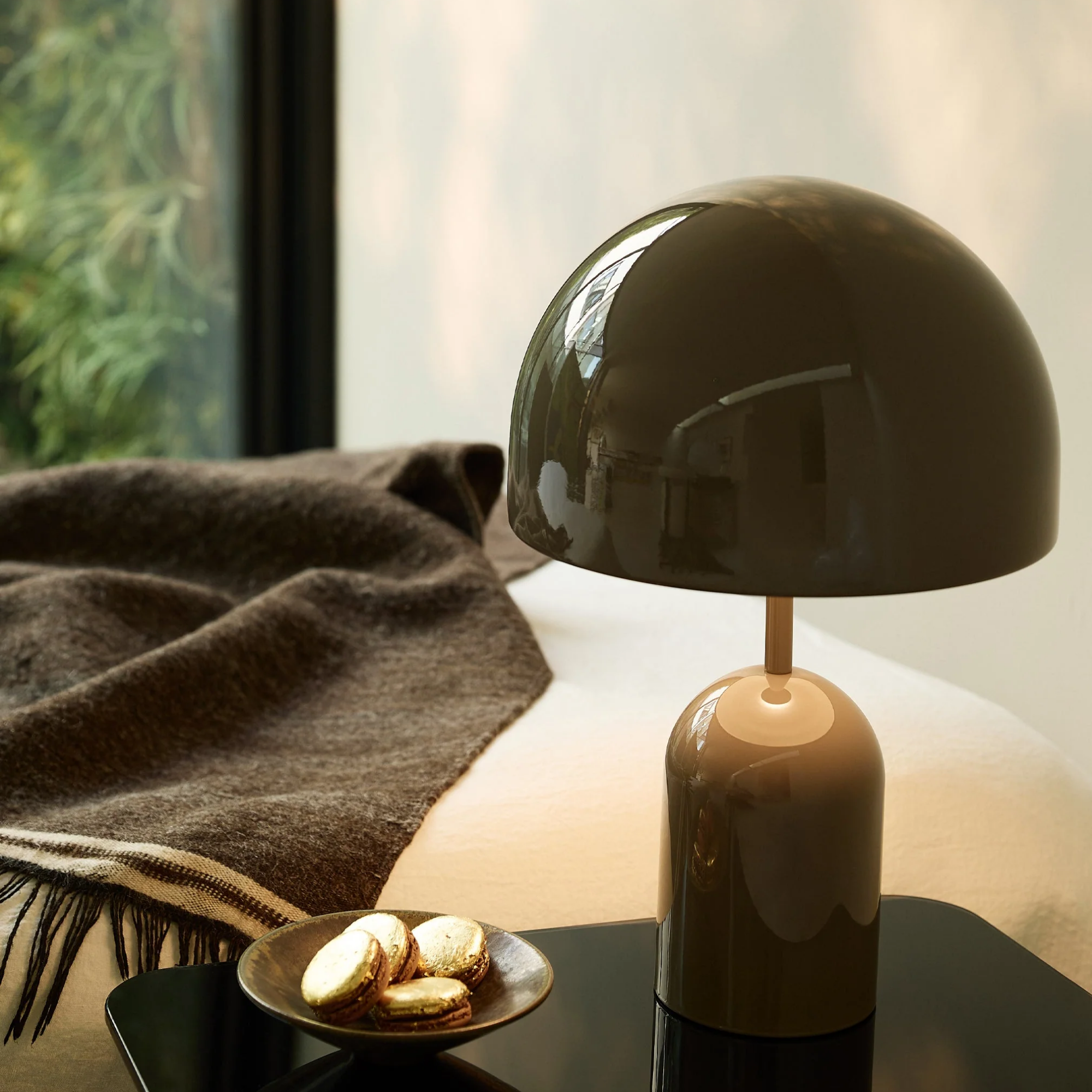 The taupe Bell Cordless Lamp from Tom Dixon inn a bedroom on a bedside table.