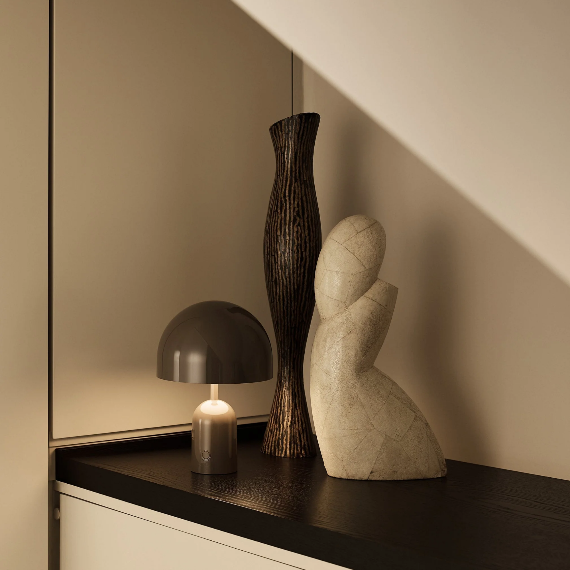 The taupe Bell Cordless Lamp from Tom Dixon in a lounge beside two art sculptures.