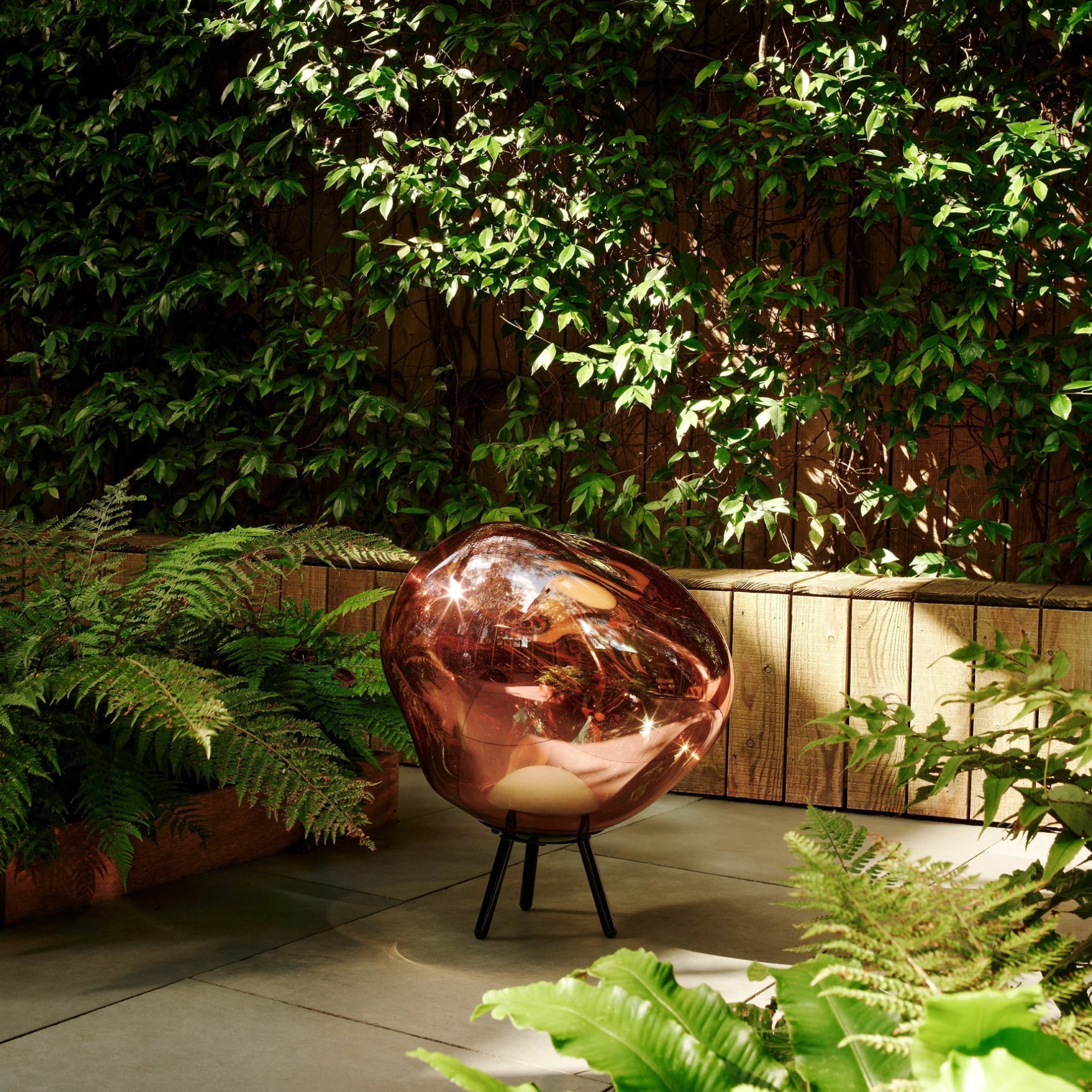 The copper Melt Cordless Floor Lamp from Tom Dixon in an outdoor living space surrounded by plants.