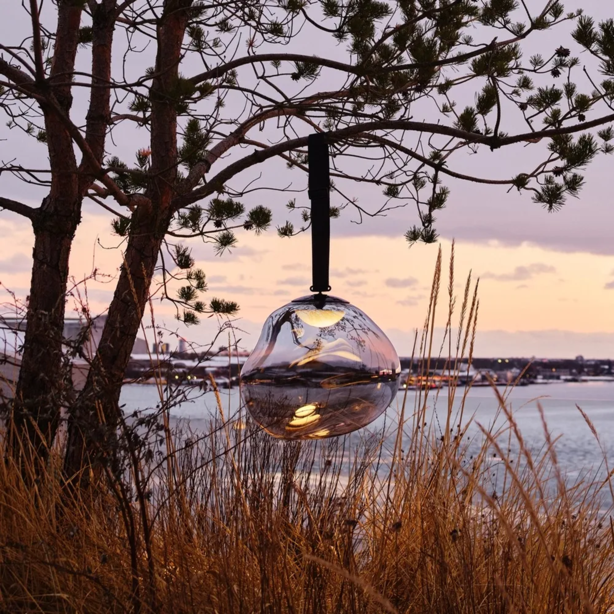 The smoke Melt Cordless Floor Lamp from Tom Dixon used at a coastal home, hung from a tree overlooking the water.