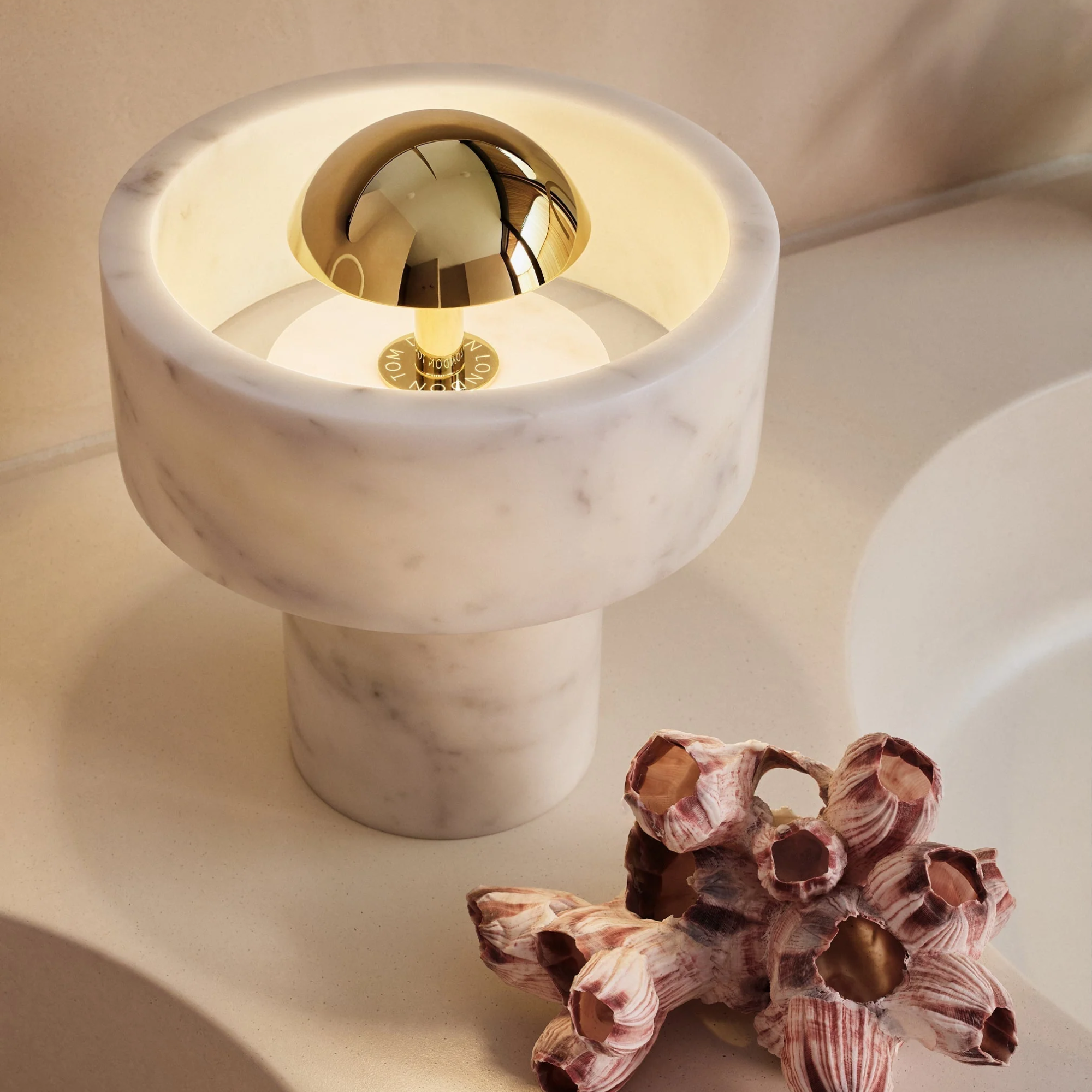 The gold Stone Cordless Lamp from Tom Dixon in a bathroom next to a sink and coral.