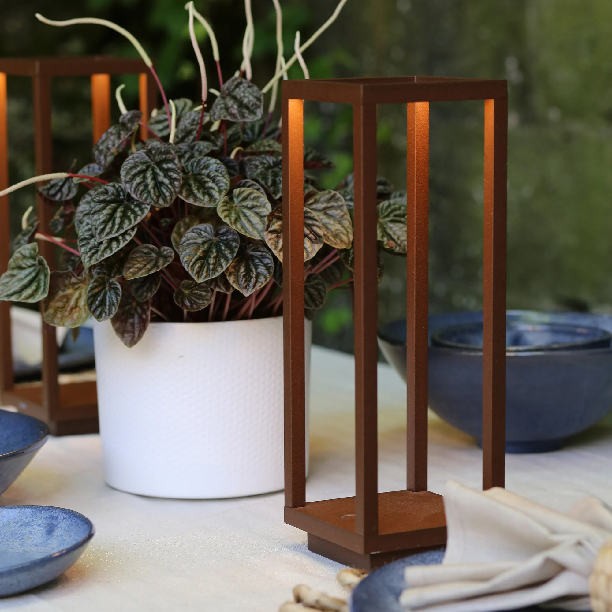 The rust Home Cordless Lamp from Zafferano on a dining table beside a plant and bowls.