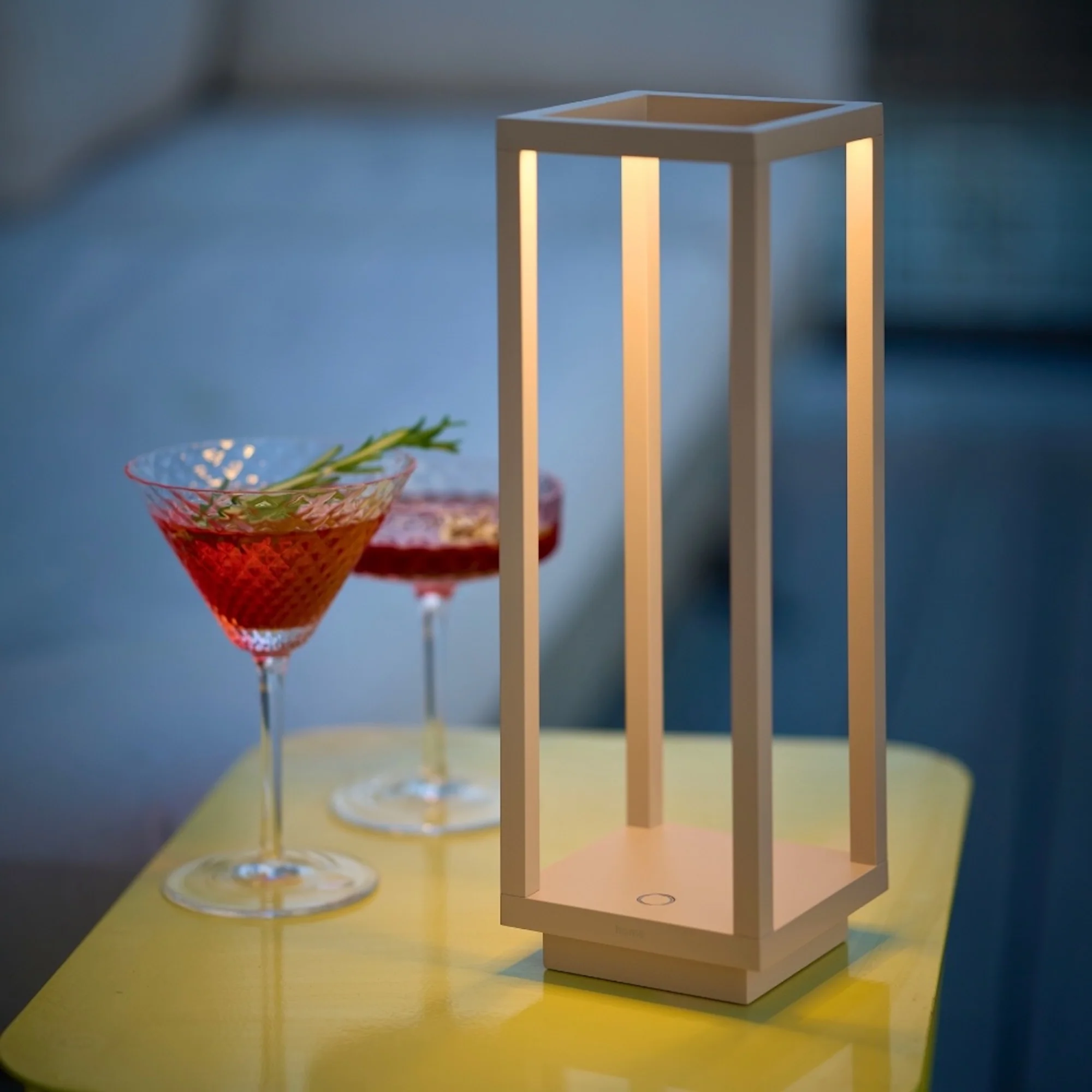 The sand Home Cordless Lamp from Zafferano in a living room on an end table next to some drinks.